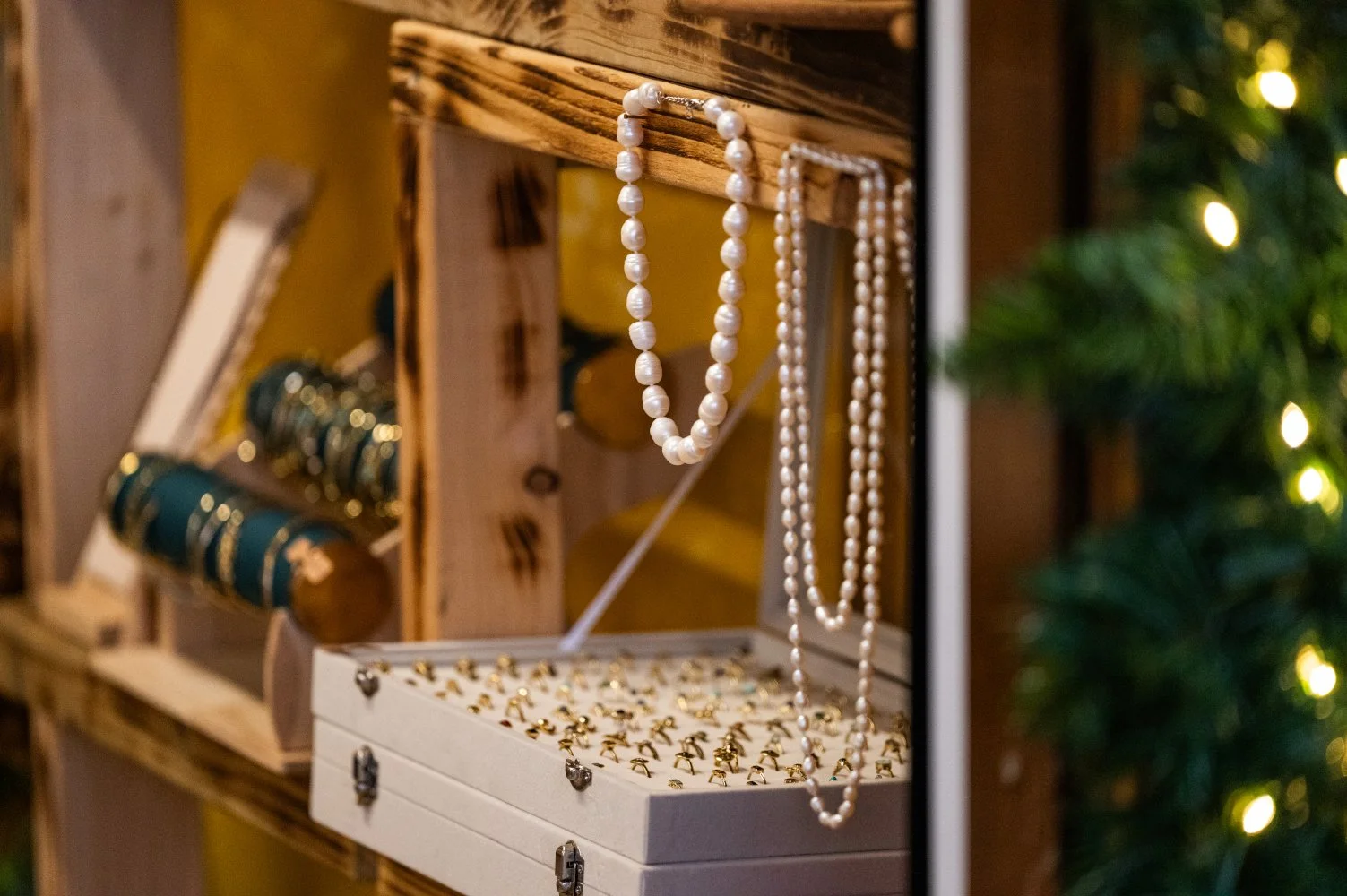 Display of pearl necklaces and rings on a jewelry stand with Christmas lights nearby.