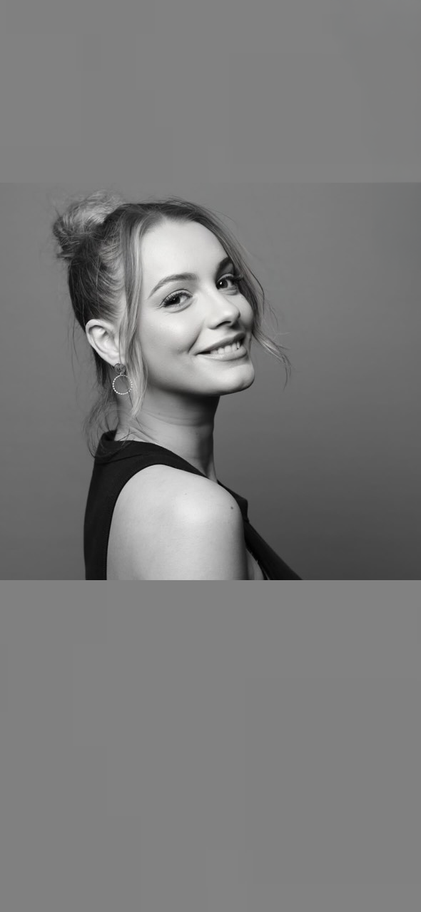 Portrait en noir et blanc d'une femme souriante avec les cheveux attachés en chignon, portant un haut sans manches et une boucle d'oreille.