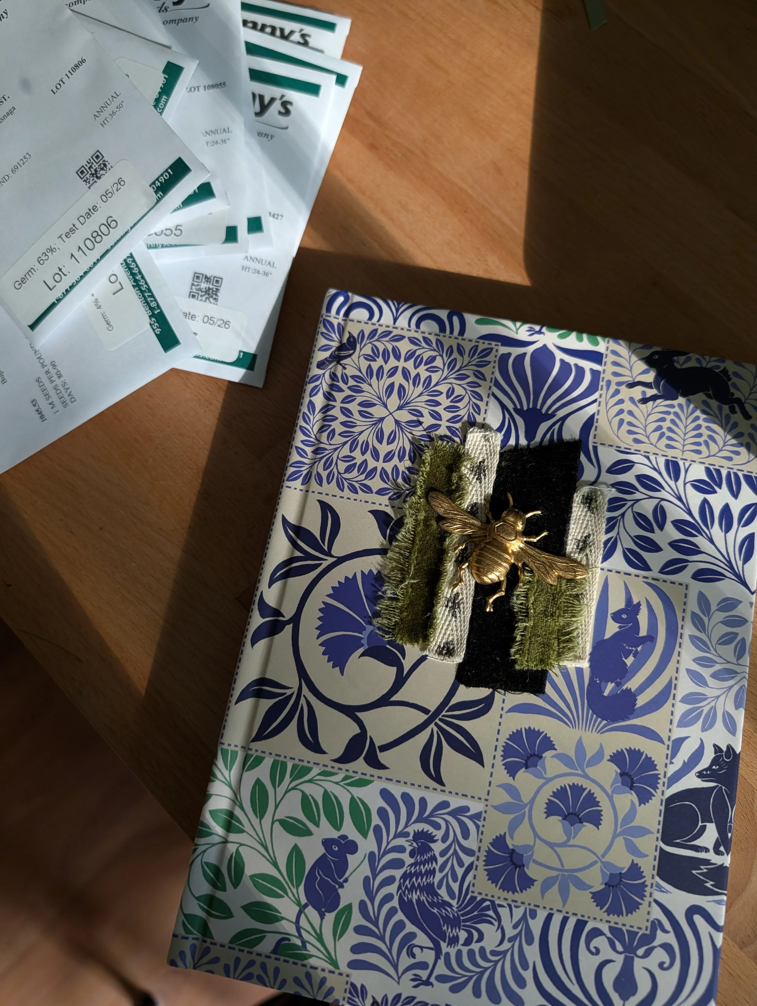 Blue and white floral patterened journal and seed packets on a wooden table while planning next season's flower varieties at Quinnfield Gardens in Athens, Tennessee.