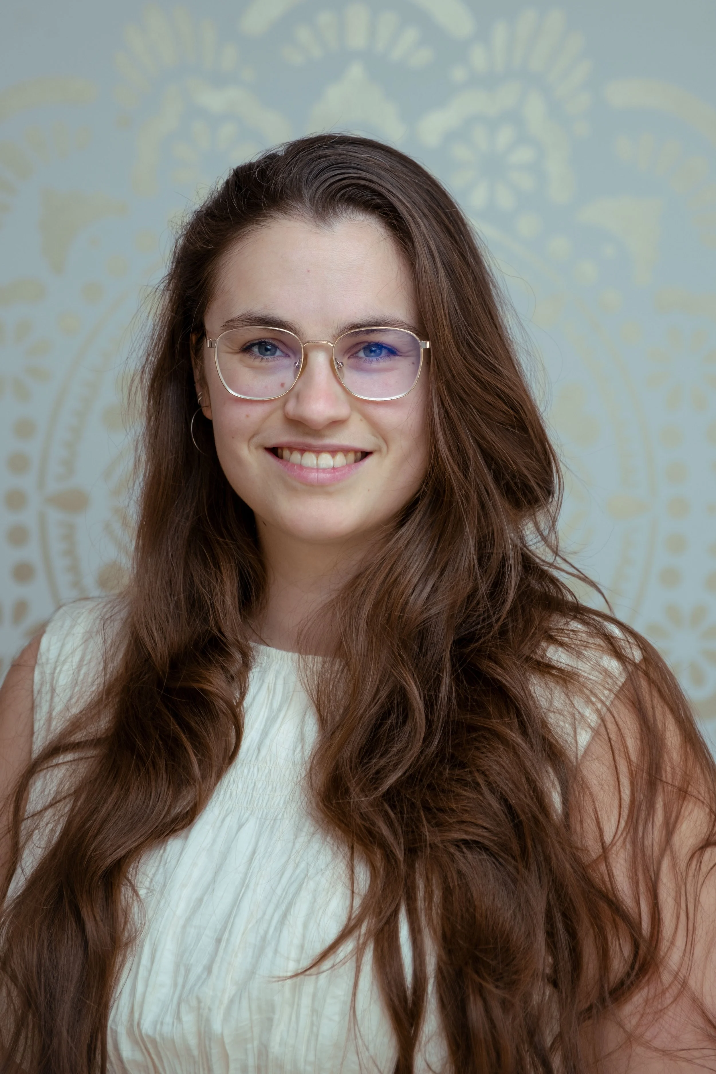 Smiling woman with long brown hair and round glasses in close-up portrait