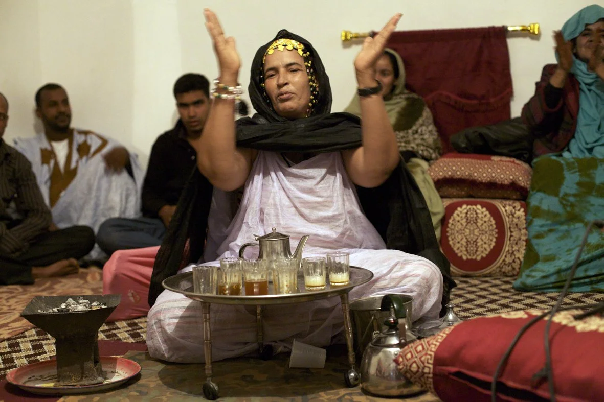 A woman dressed in traditional attire performing a dance during a gathering, surrounded by seated people in a decorated room.