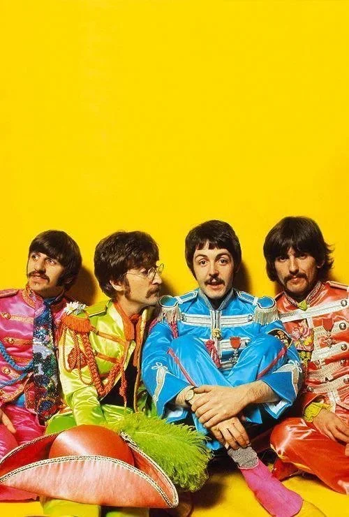 The Beatles in colorful military-style uniforms, sitting against a yellow background.