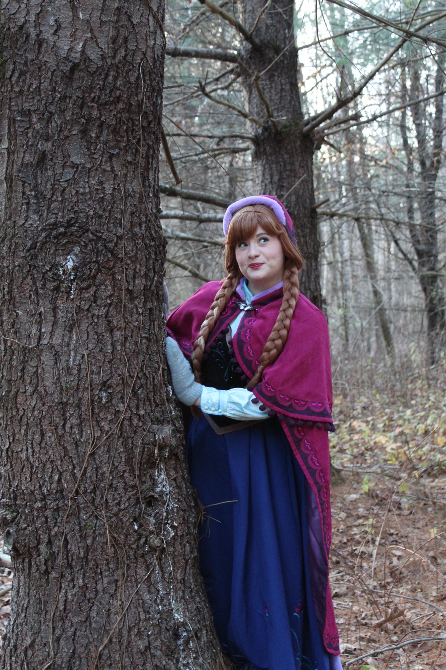A woman dressed as Princess Anna from Disney's Frozen, with braided hairstyle, wearing a black and green bodice with embroidered designs, in an outdoor setting with greenery and trees in the background.