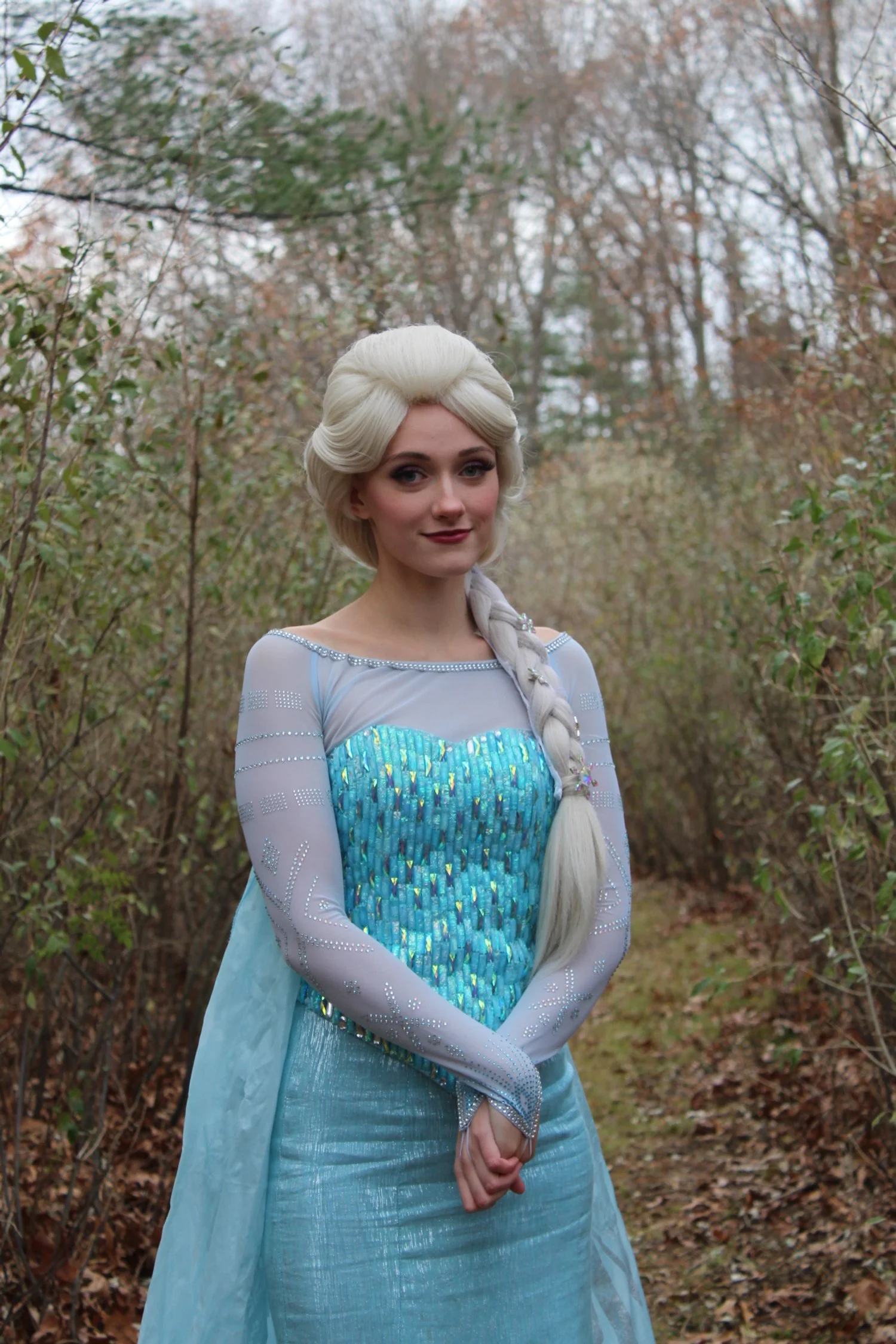 Young woman dressed as Elsa from Frozen posing in front of a light blue wall decorated with star and police badge stickers.