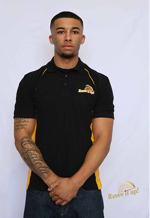 Young man with short black hair, wearing a black polo shirt with yellow accents and a logo, standing against a light background, with tattoos on his left arm, looking at the camera.