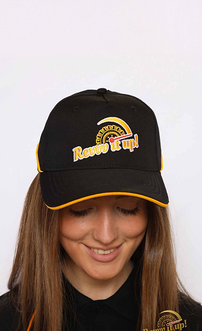 Young woman wearing a black baseball cap with yellow accents and logo, smiling with eyes closed.