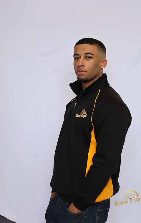 Young man with short hair and a goatee wearing a black and yellow jacket, standing against a plain white background.