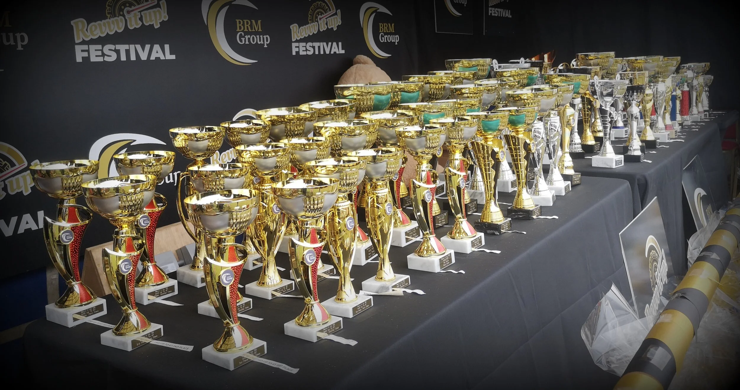 A large display table filled with numerous gold, silver, and trophy-style awards at a festival or competition event.