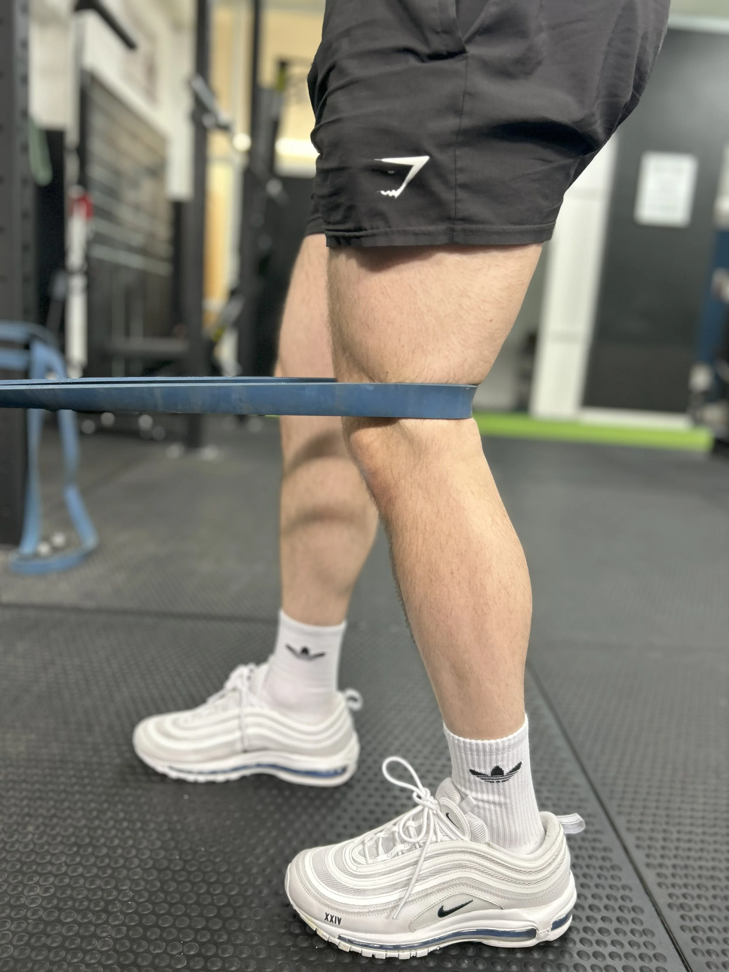 A person wearing white Nike sneakers and performing resistance band exercises in a gym.