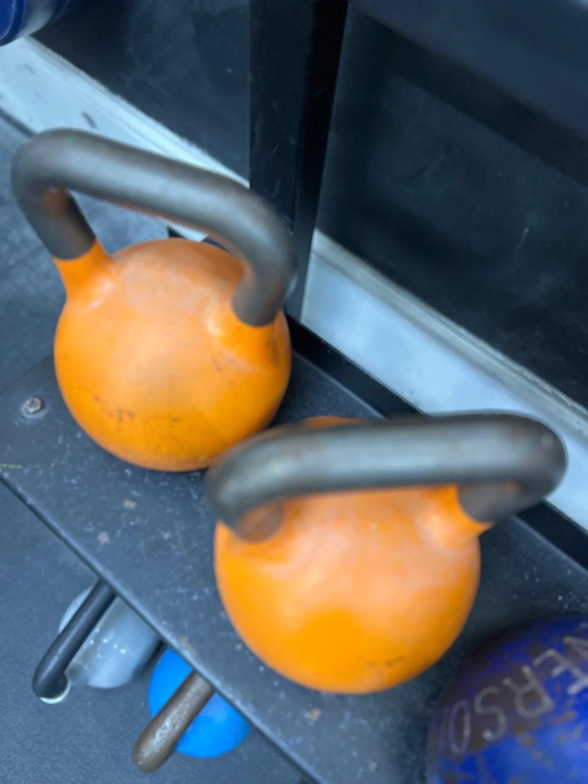 Two orange kettlebells placed on a black gym floor.