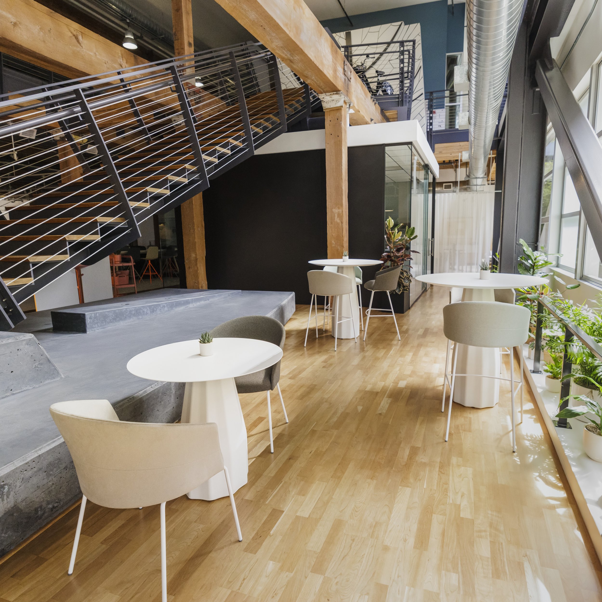 Modern indoor cafe or lounge with wooden flooring, white and beige tables, and chairs.