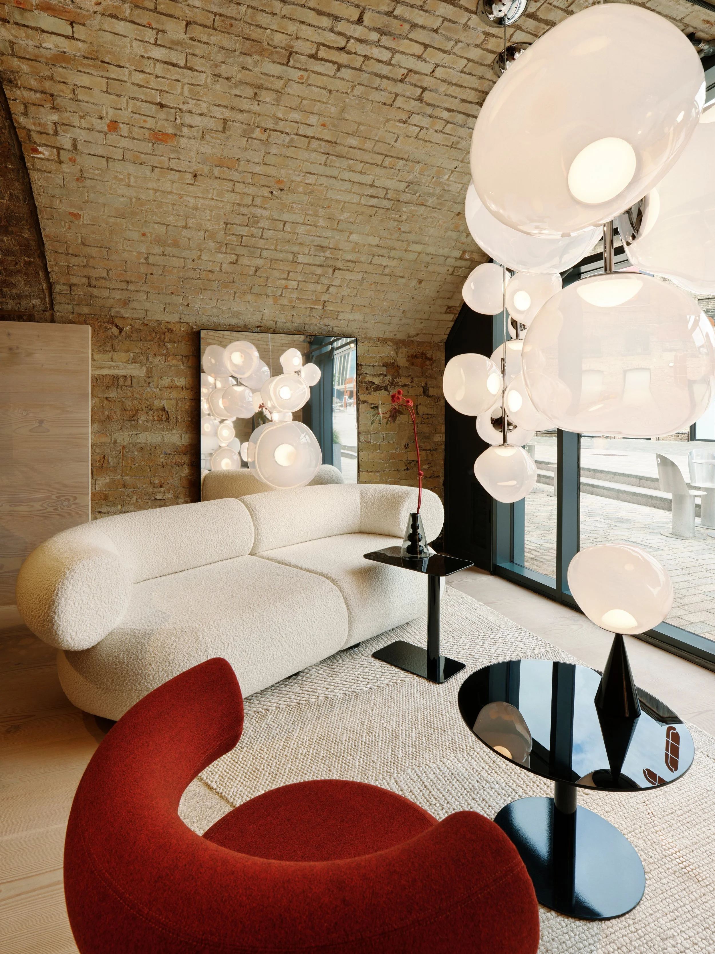 Modern lounge area or lobby featuring Tom Dixon furniture with a textured white sofa, red curved chair, black and white tables, and unique hanging and table lamps with white glass globes.