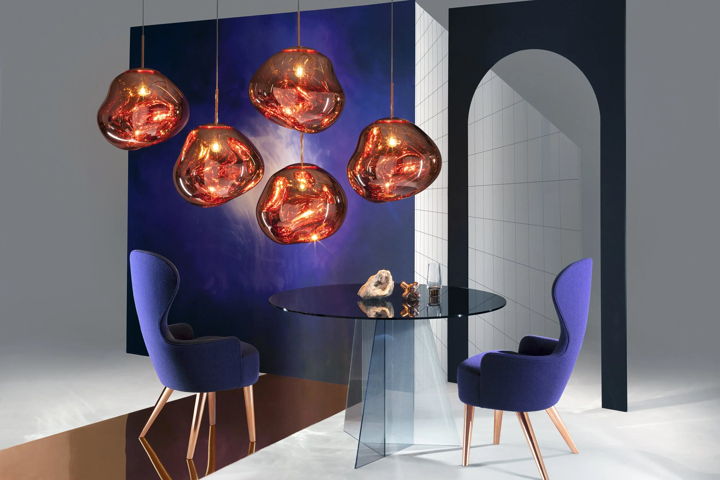 Modern dining area with a black glass table, two purple upholstered chairs with wooden legs, and a cluster of five copper-colored pendant lights hanging above.