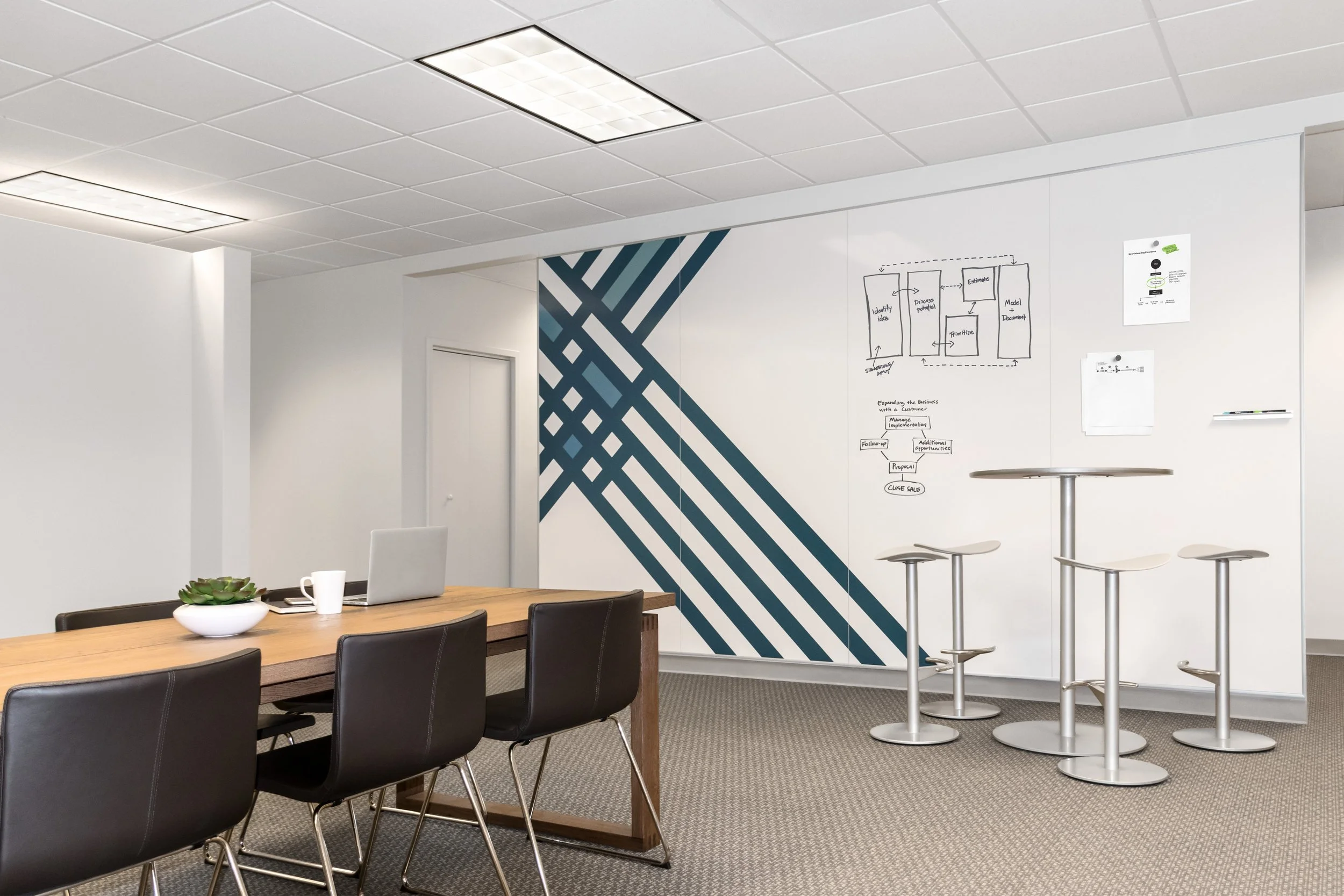 Modern conference room with a wooden table, black chairs, and white PolyVision CeramicSteel walls used as writable whiteboards.