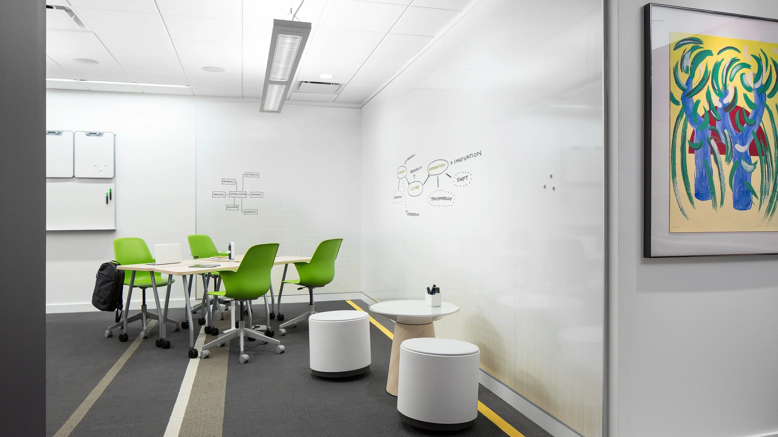 Study and meeting space in a school with green chairs, a white table, and a full PolyVision CeramicSteel wall used as a large whiteboard for student collaboration.