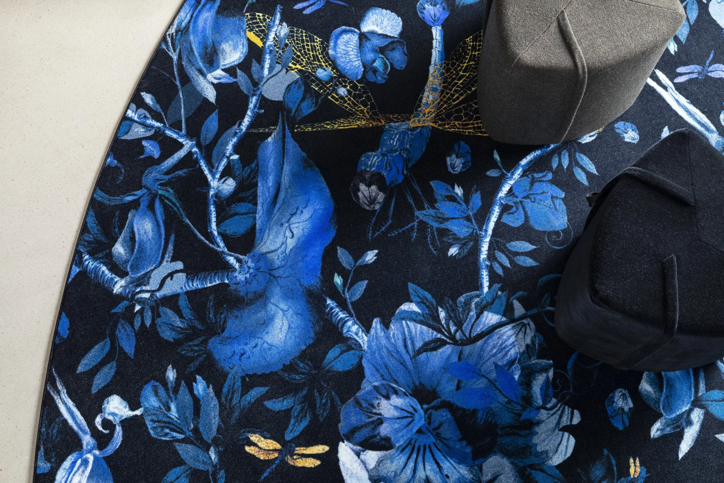 Close-up of a round Moooi Carpets carpet with a unique blue floral and animal pattern, featuring branches, leaves, flowers, and a bird.