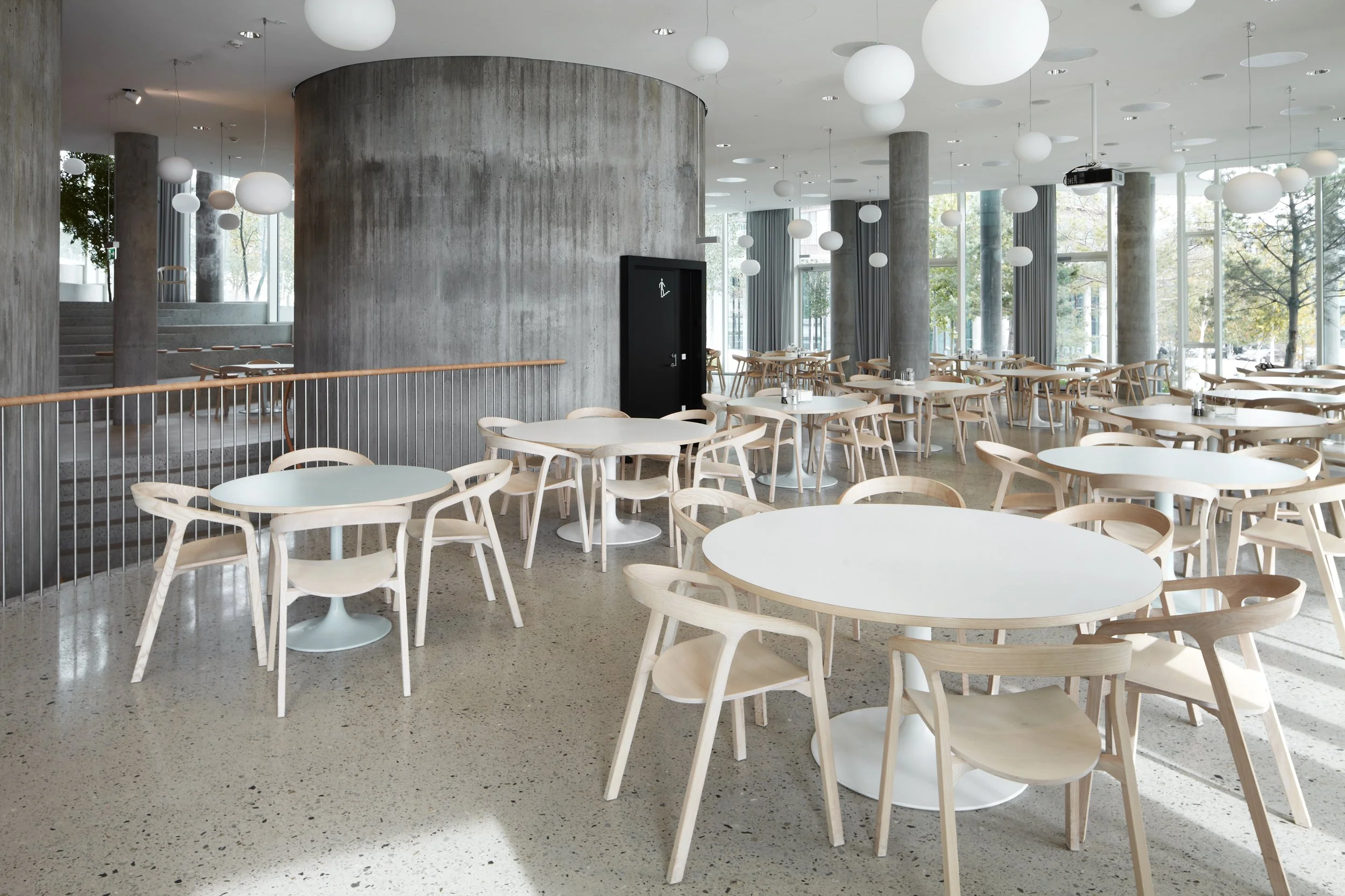 Restaurant with white round tables and wooden chairs by Mattiazzi.