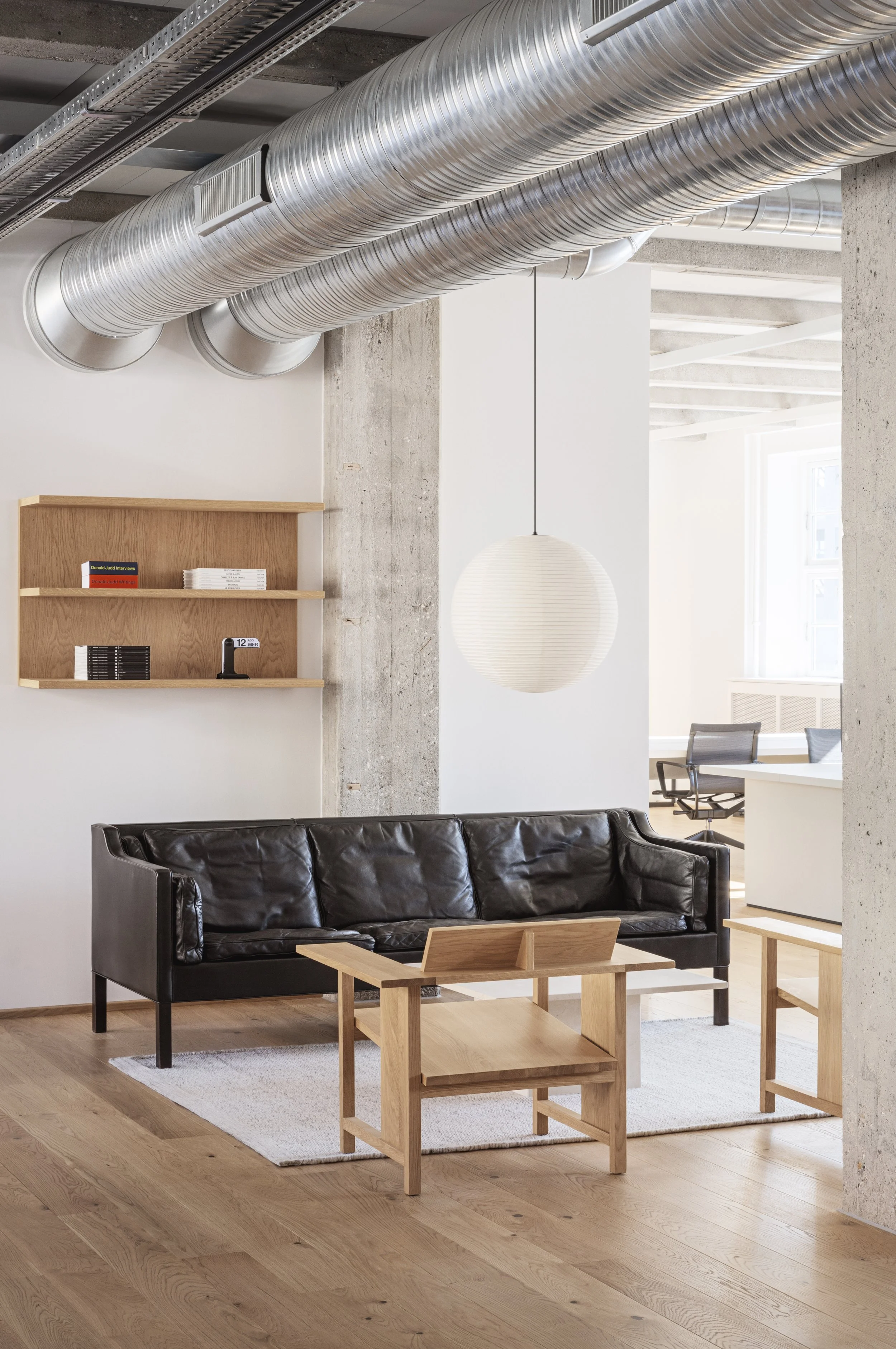 Lounge area with black leather sofa, wooden coffee table, and wooden shelf on wall.