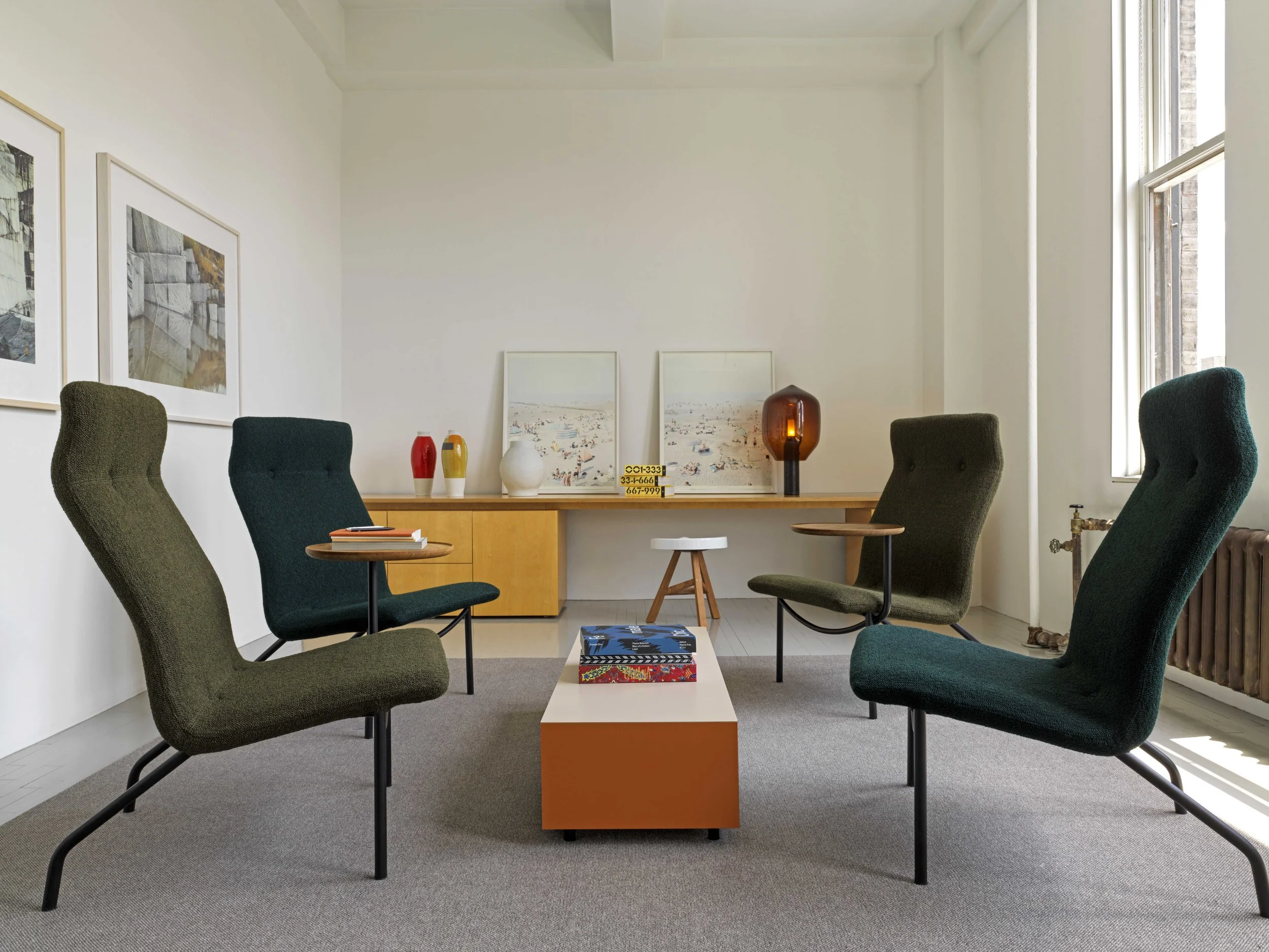 Lounge area with upholstered chairs, a low coffee table, and a wooden sideboard with decorative vases and framed artwork.