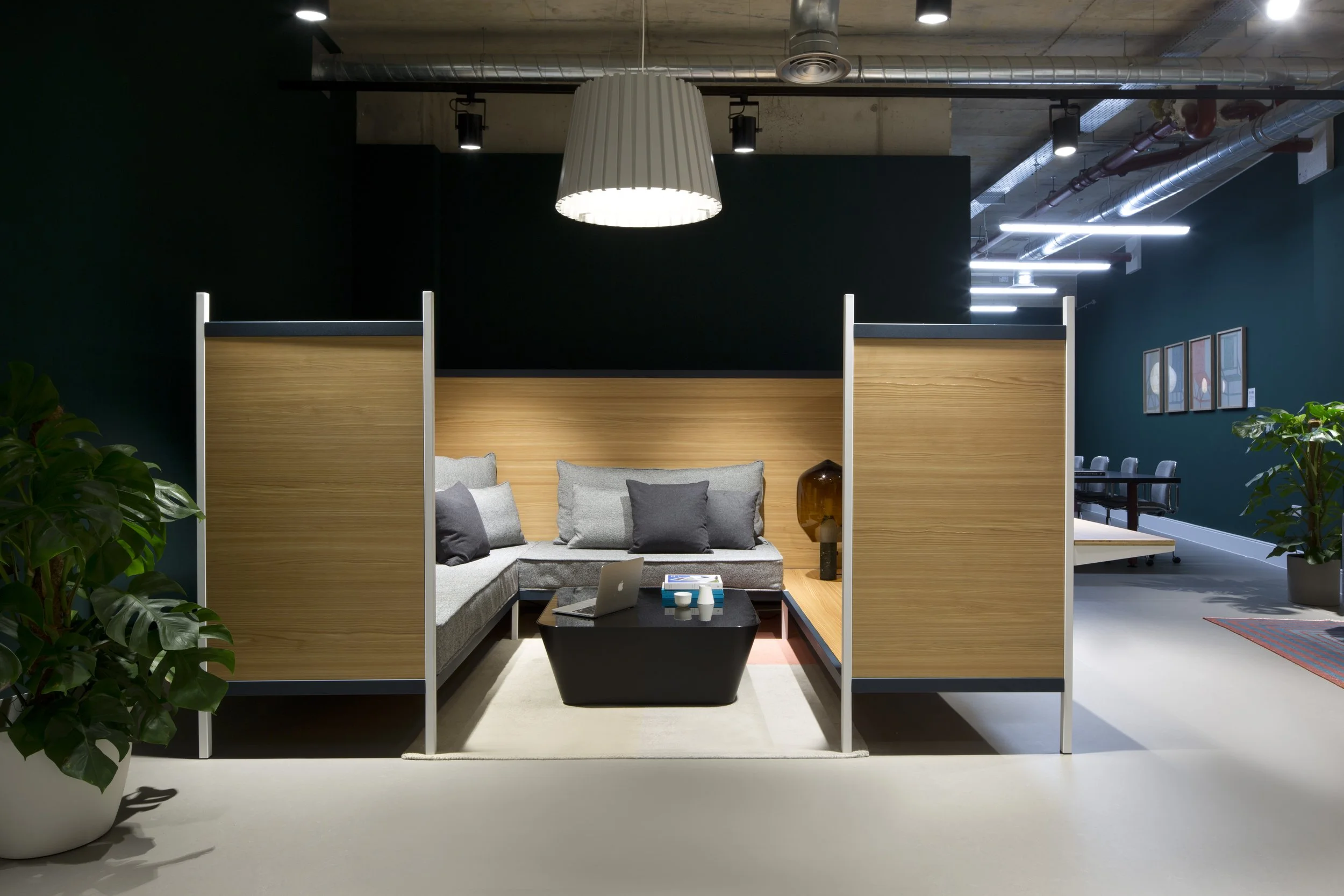 Modern coworking space with a cozy seating area enclosed by wooden partitions, featuring a gray sofa with cushions, and a black coffee table.