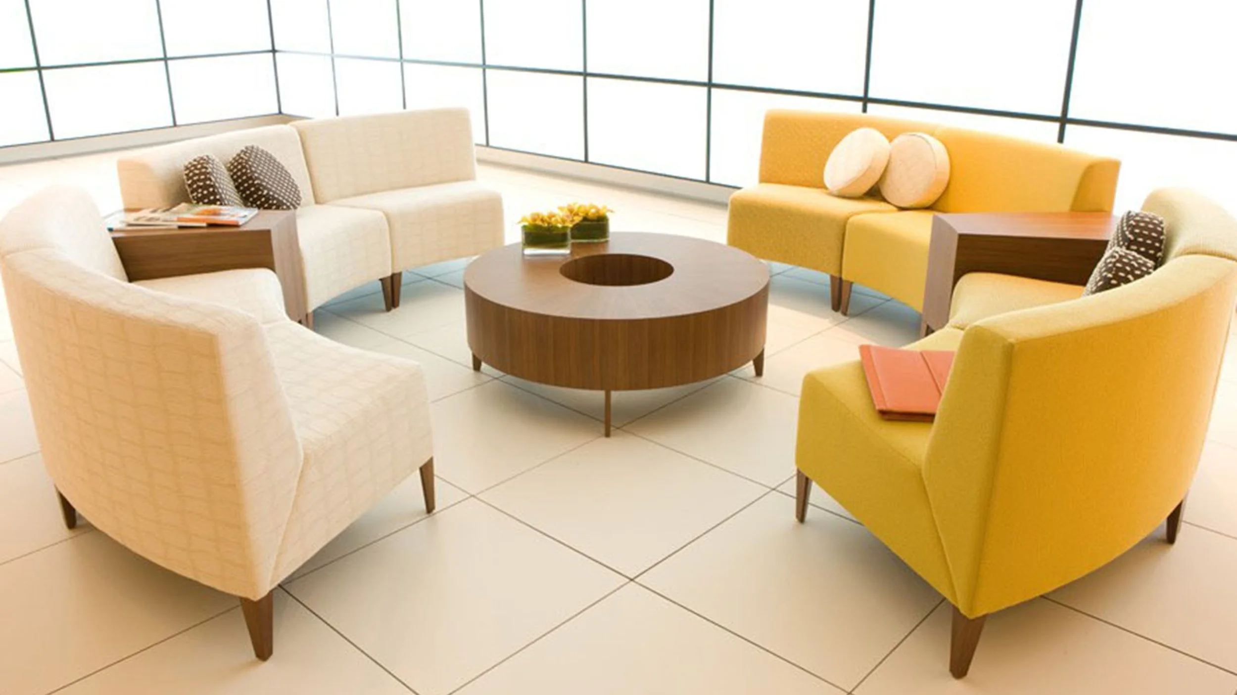 Lounge area with colorful chairs by Coalesse, arranged around a circular wooden coffee table.