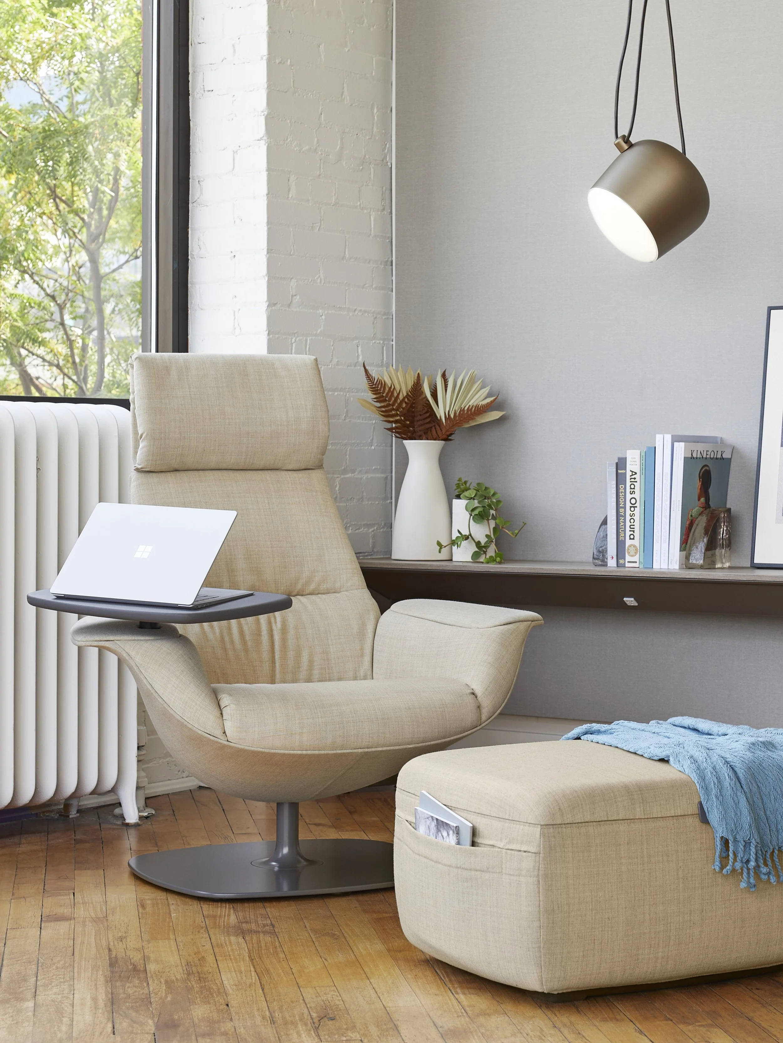 Office rejuvenation area featuring a beige swivel chair, ottoman, floor lamp, and bookshelf.
