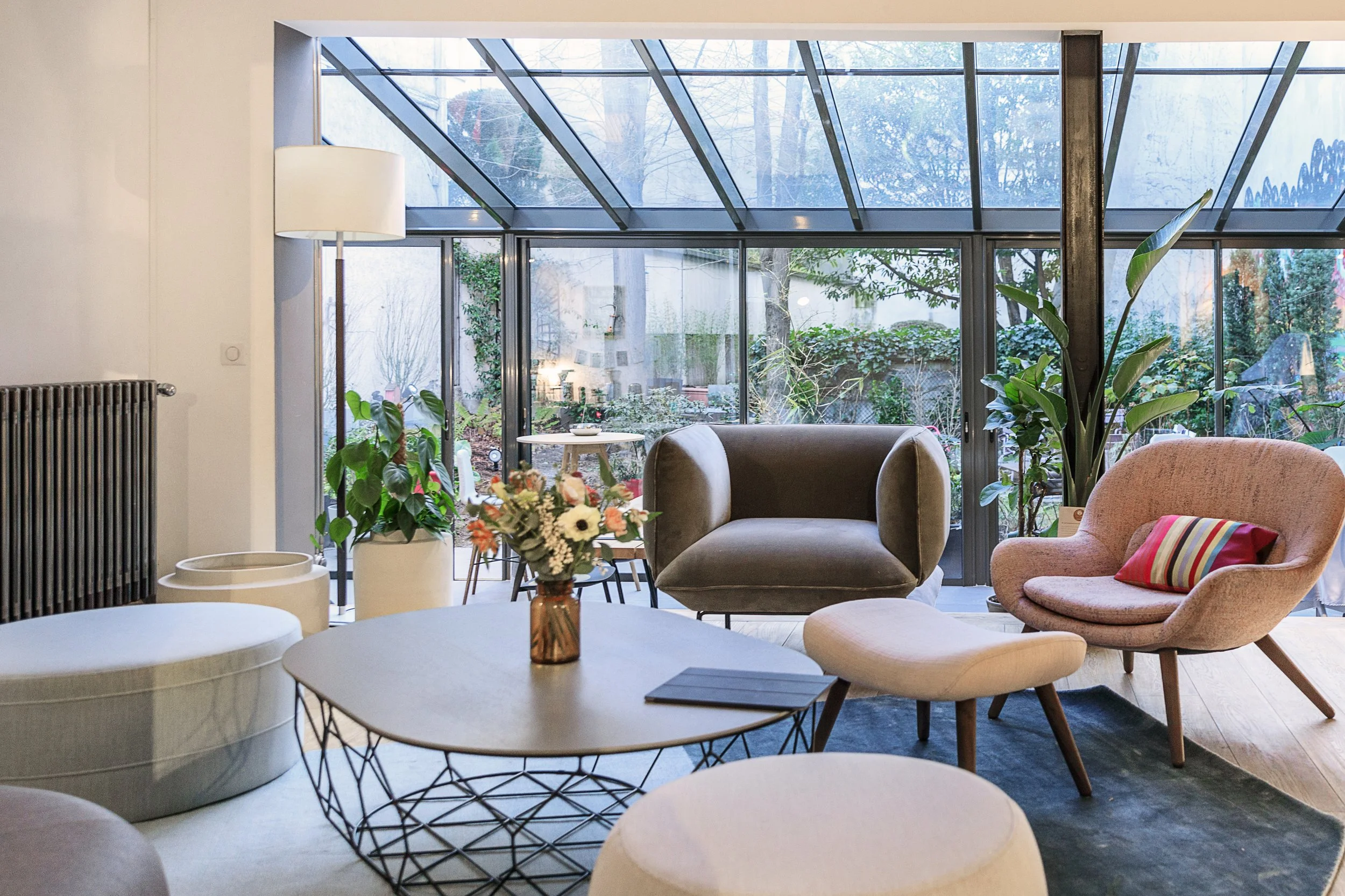 Lounge area with modern furniture from Bolia, including a pink armchair with a striped pillow, a grey rounded armchair, a white ottoman, and a coffee table.