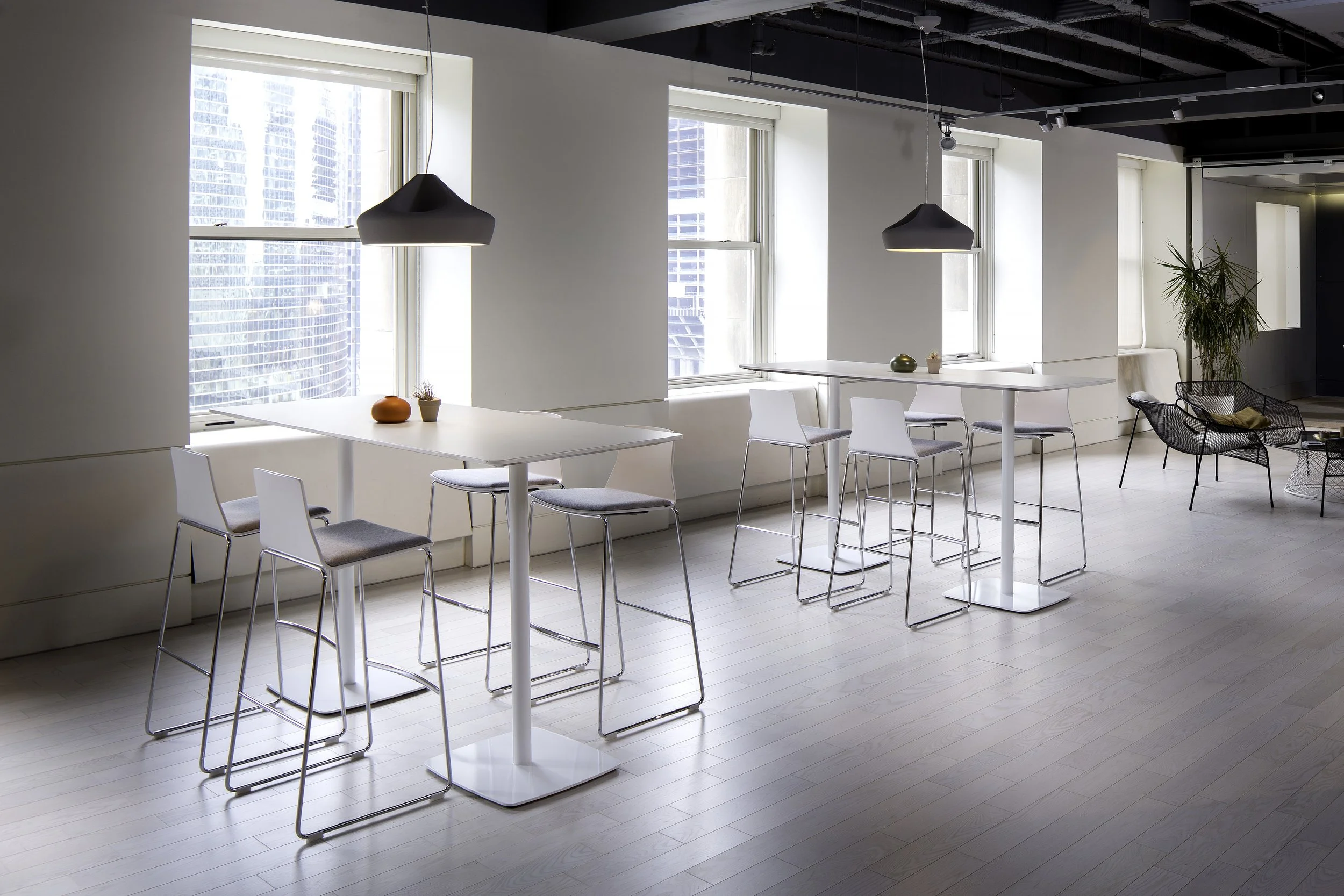 Modern bright office lounge with white tables, chairs, and pendant lighting.