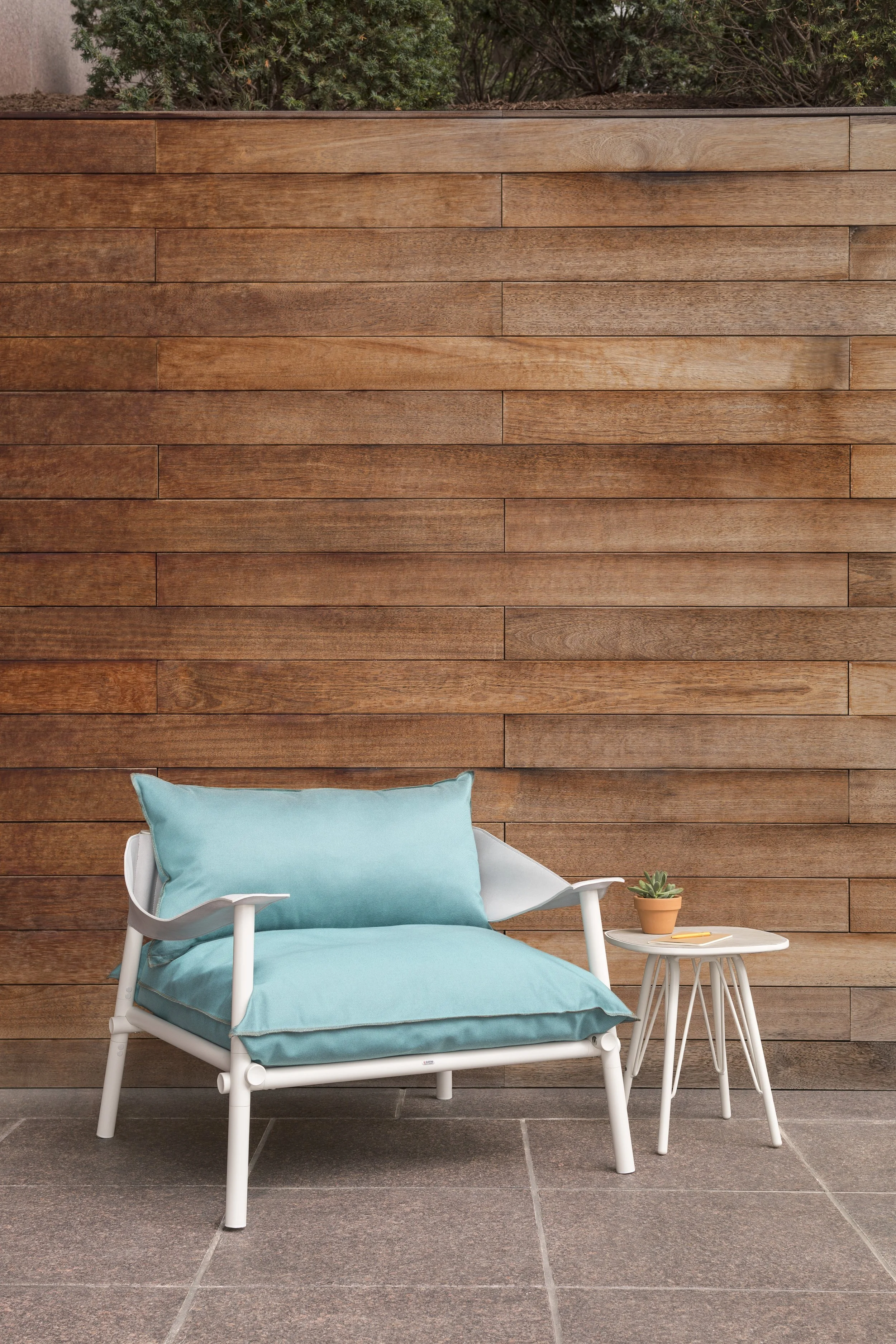 Outdoor patio with a modern white Emu lounge chair featuring light blue cushions and matching pillow, accompanied by a small white side table.