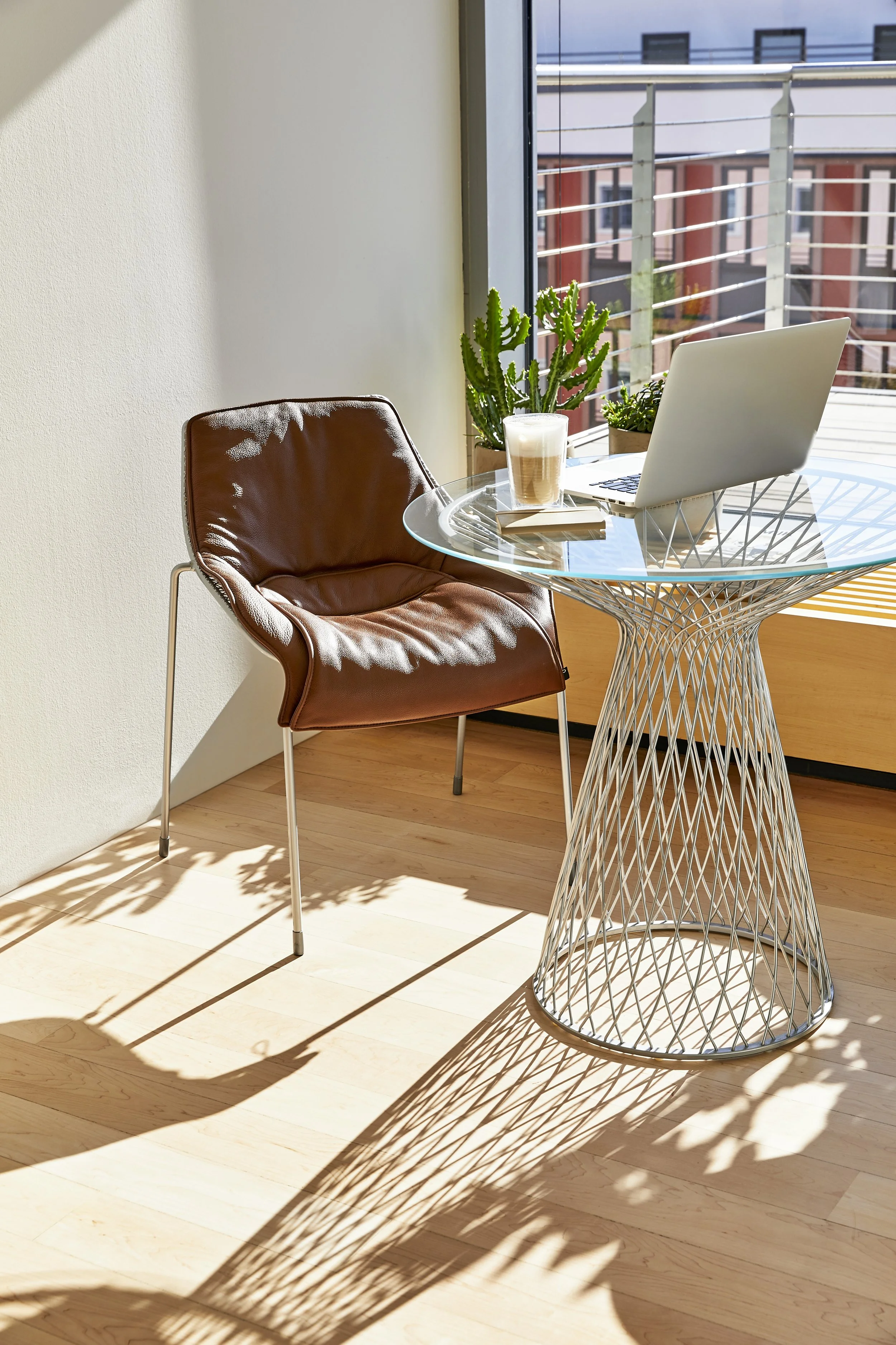 Cozy corner featuring a glass-top wireframe table and a brown leather chair.