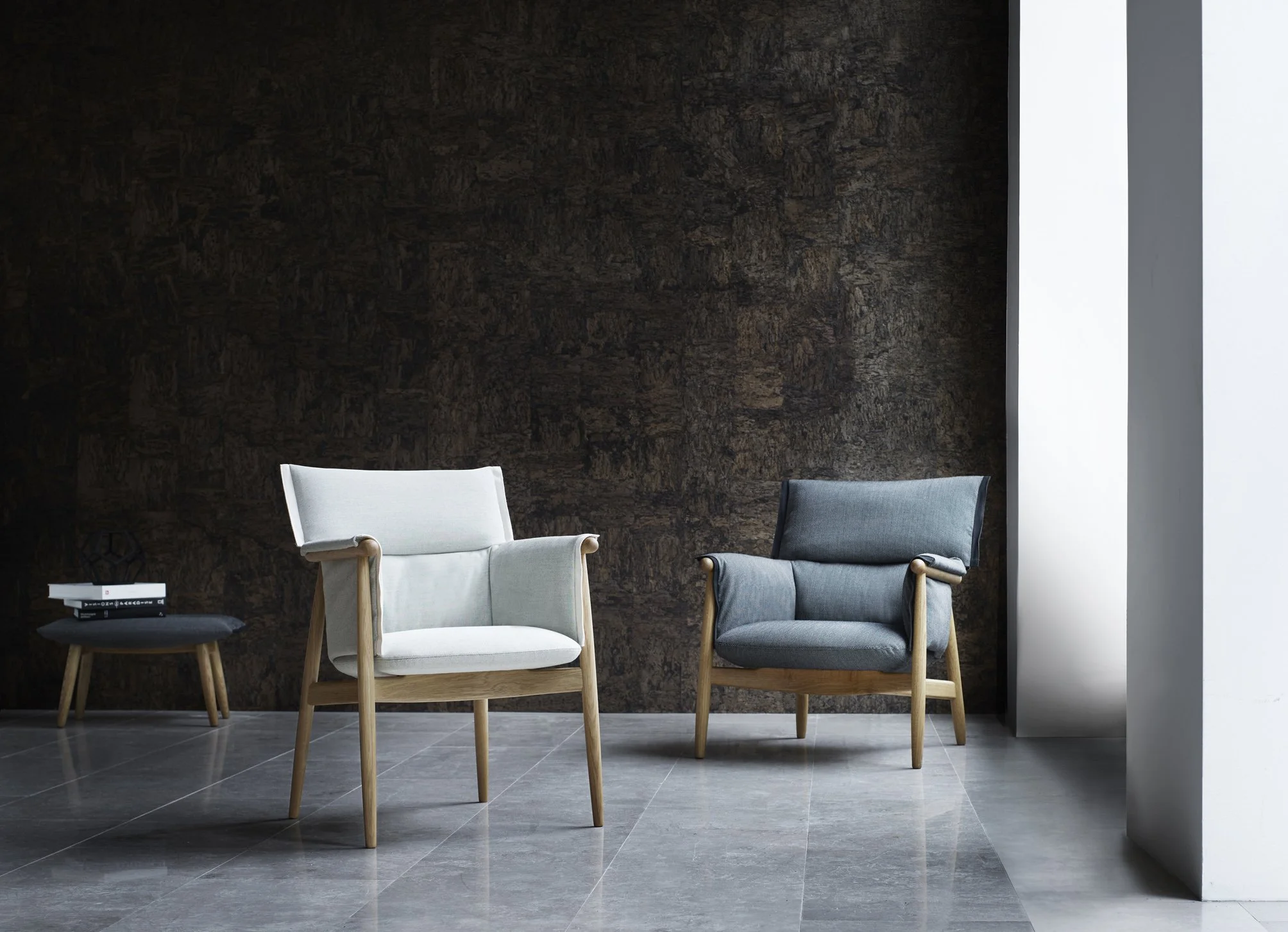 Modern lounge area with two armchairs featuring wooden frames and fabric cushions, and a small round black side table holding books.