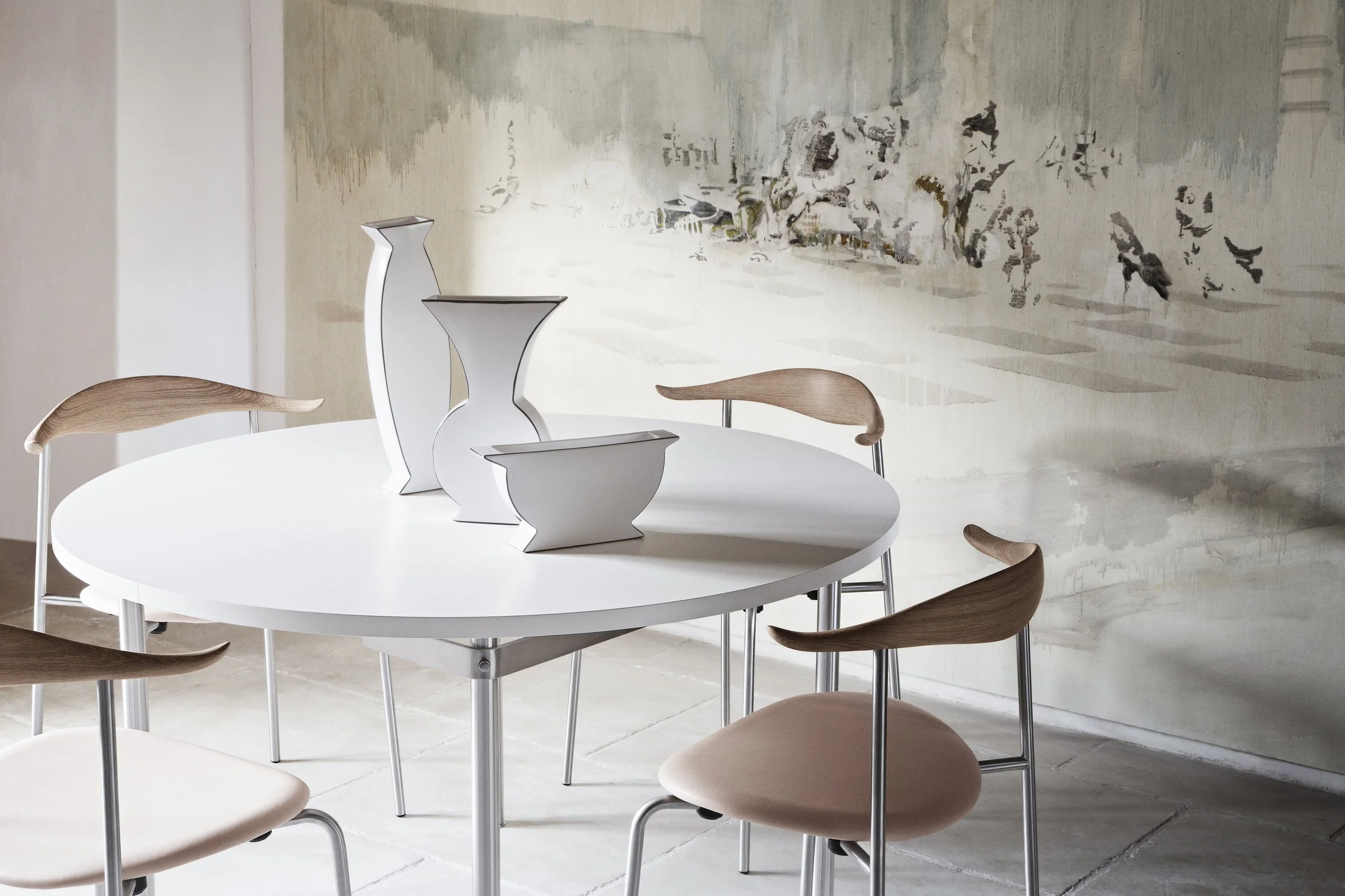 Modern dining area with a round white table and wooden chairs.