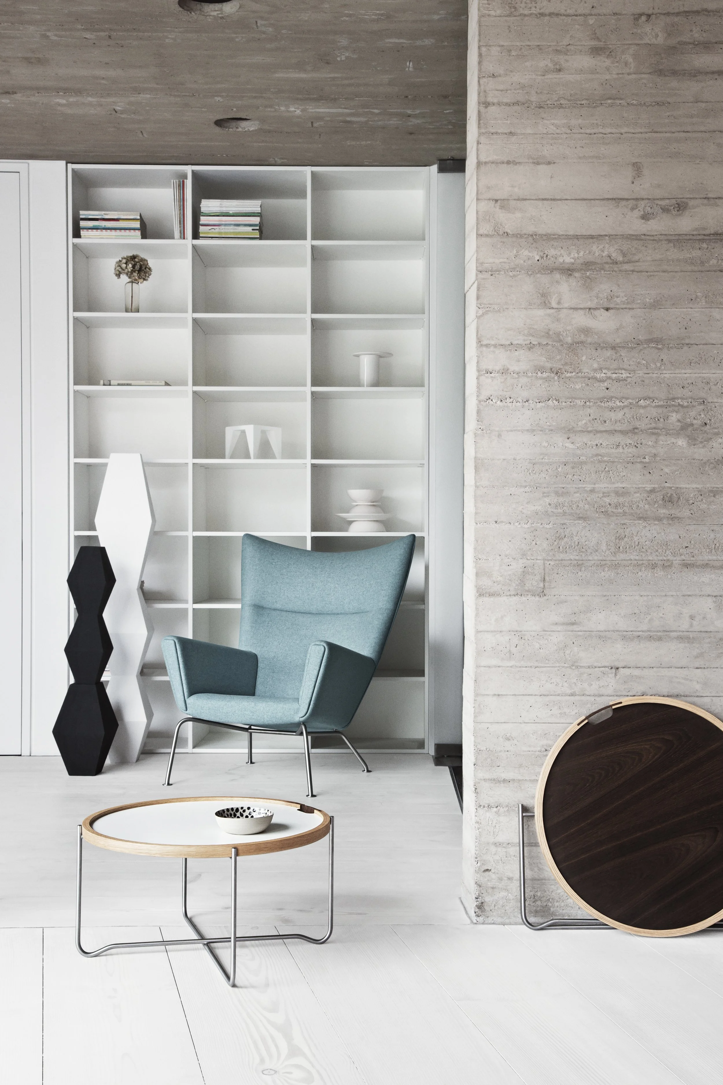 Modern sitting area with a light blue armchair, a round wooden coffee table, and a white bookshelf.