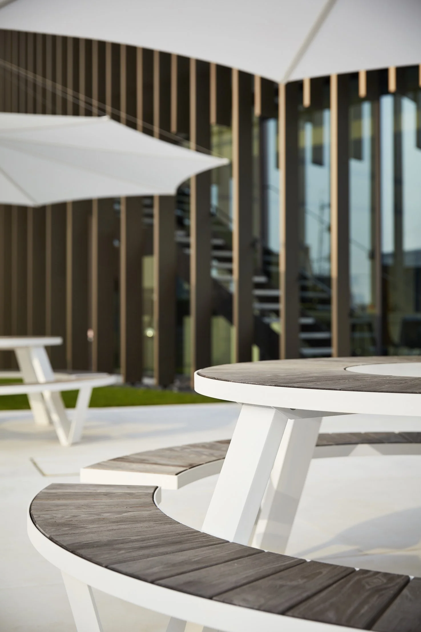 Outdoor patio area featuring curved wooden and white tables with white umbrellas from outdoor furniture manufacturer Extremis.