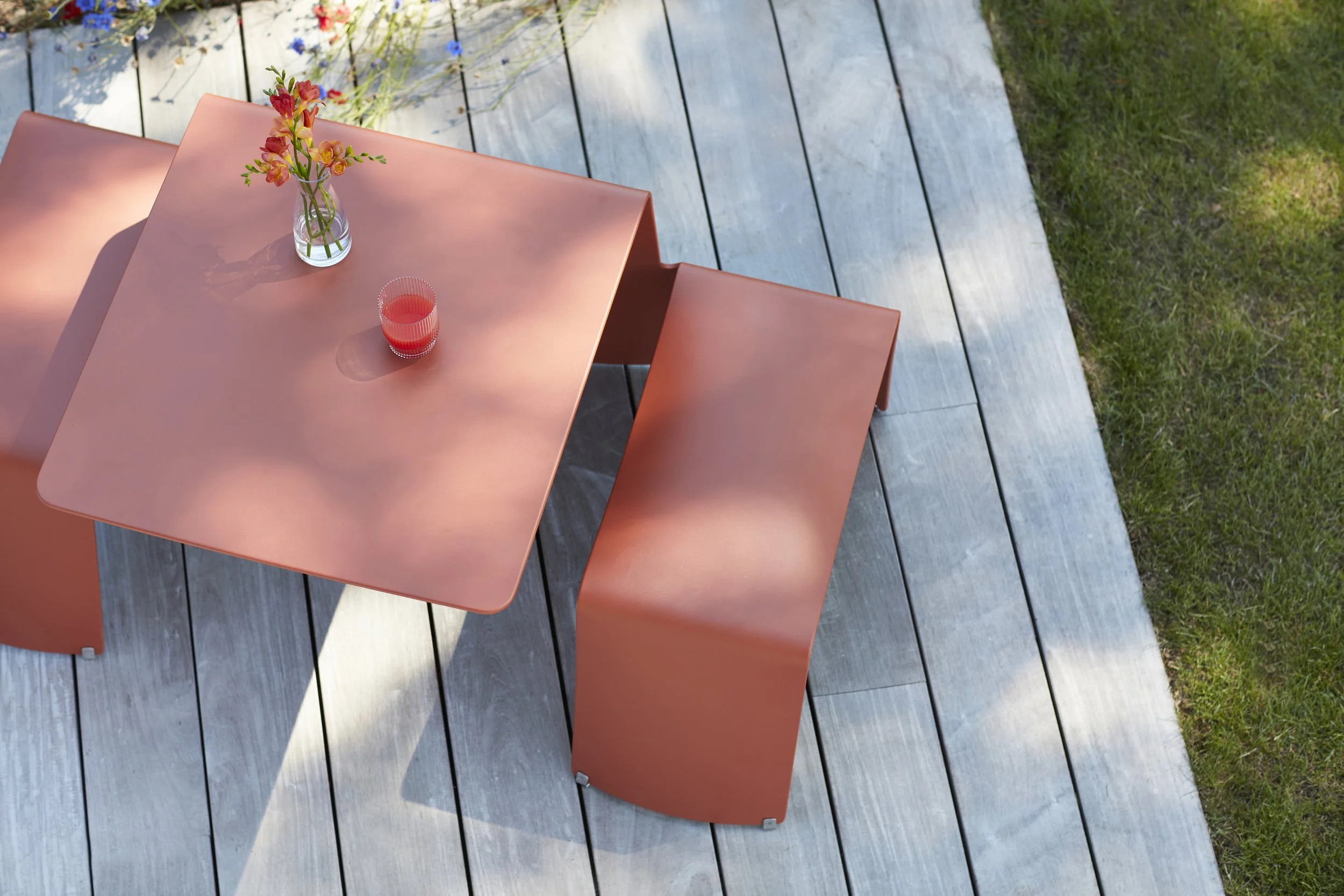 Modern outdoor dining table with a smooth matte orange finish and matching curved chairs, designed by Extremis.