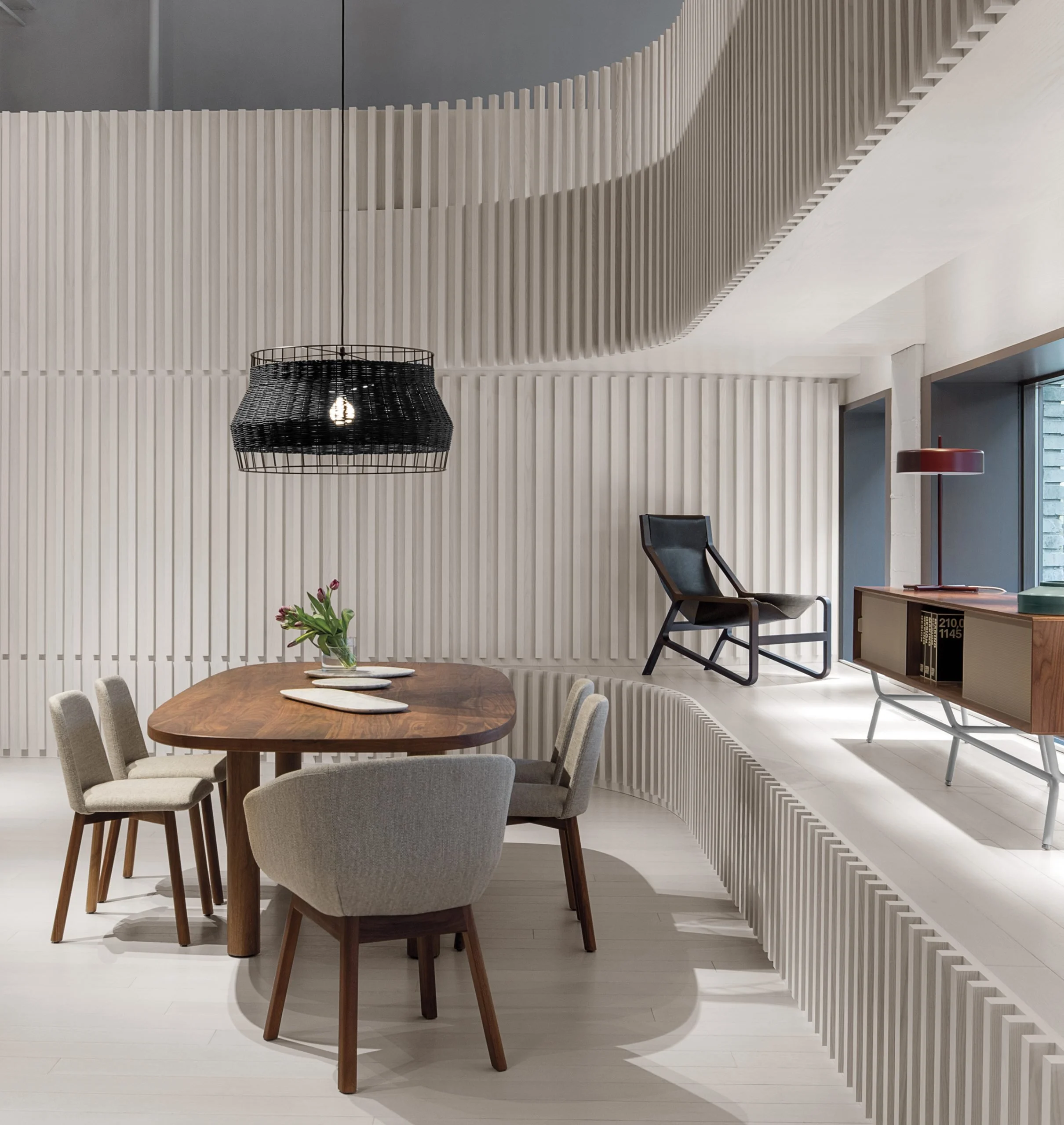 Modern dining area with a wooden table, six upholstered chairs, a black lounge chair on a ledge, and a console table from Blu Dot.