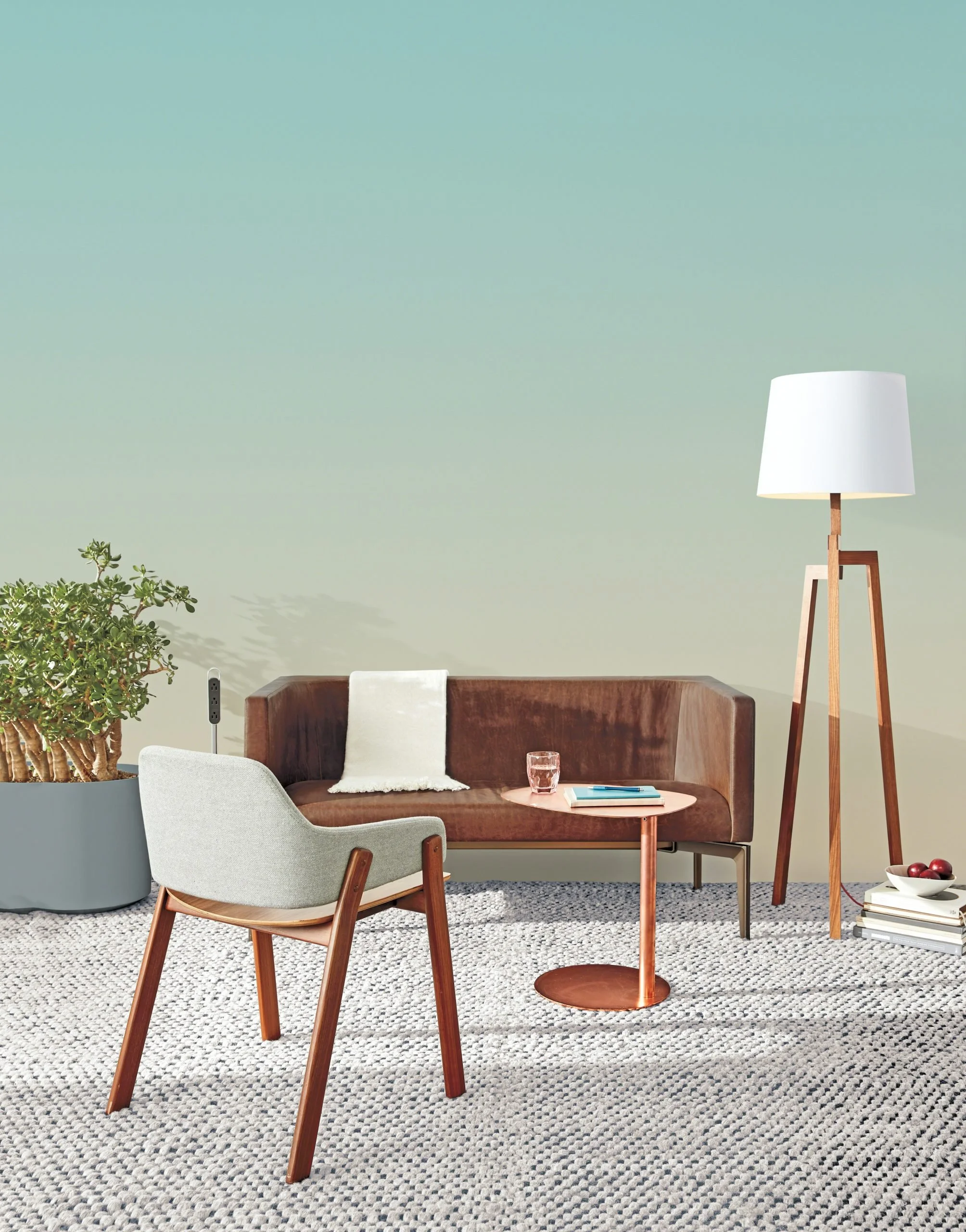 Minimalist lounge area with a brown leather sofa, white armchair, small copper side table, and tall wooden floor lamp from Blu Dot.