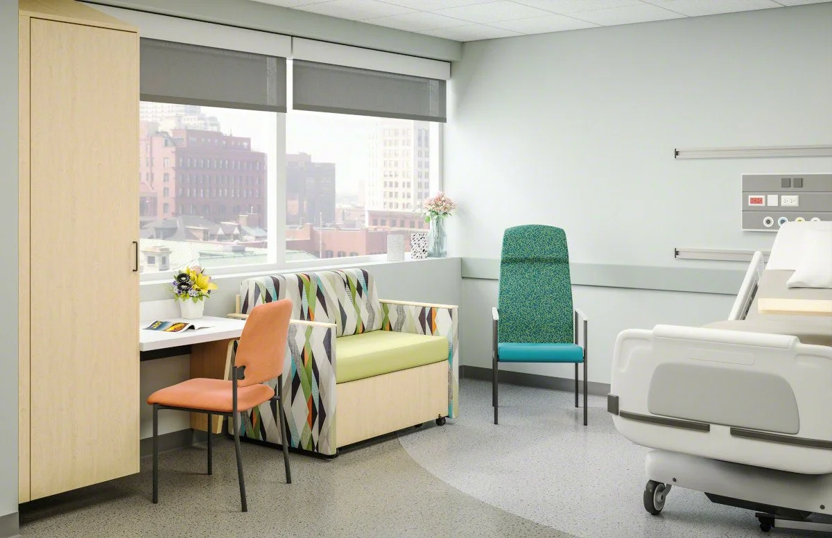 Hospital room featuring a bed, green chair, floral loveseat, desk, and casework with cabinet, furnished with Steelcase Health products.