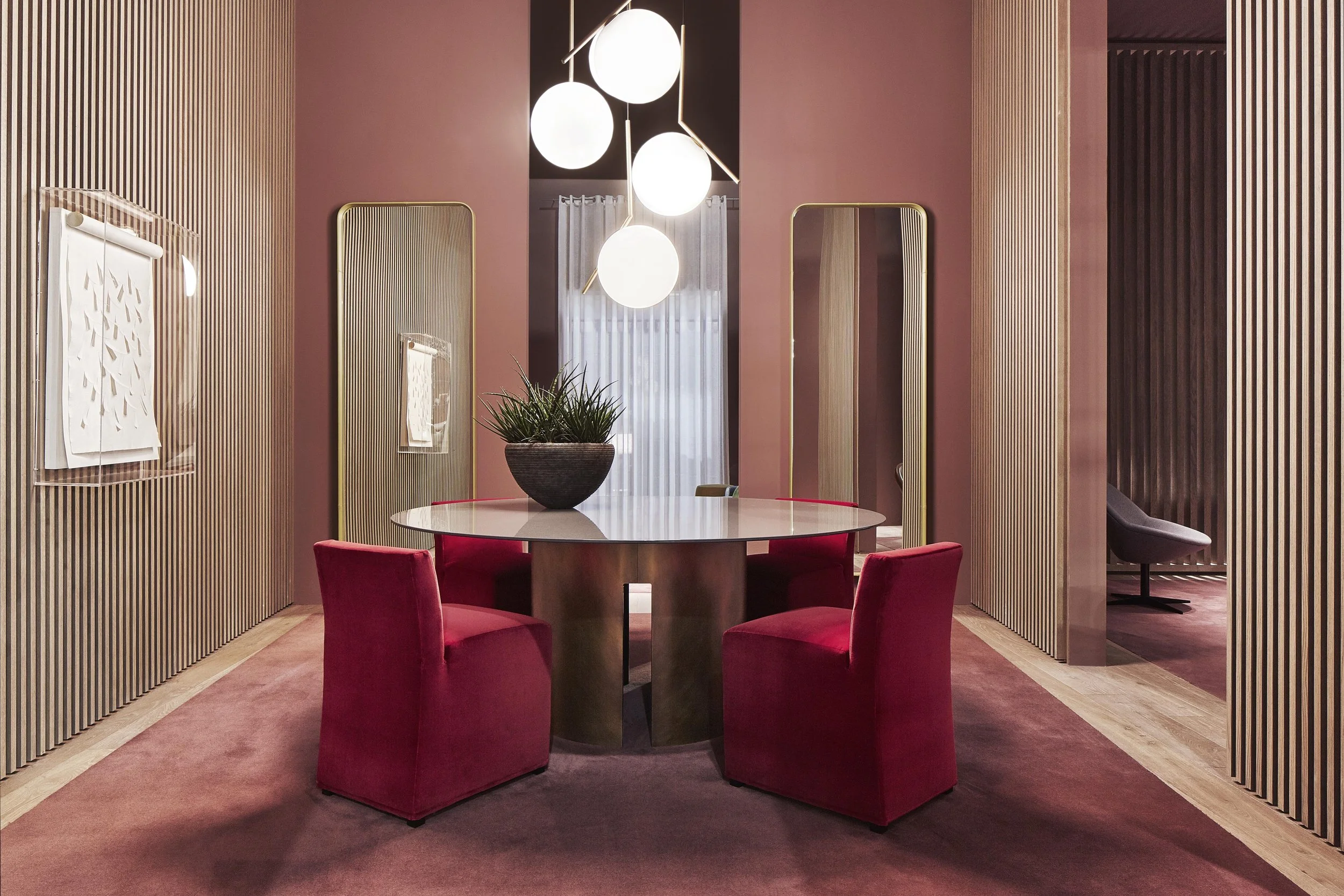 Modern dining area with a round marble table, four red upholstered chairs, and hanging globe pendant lights by FLOS.