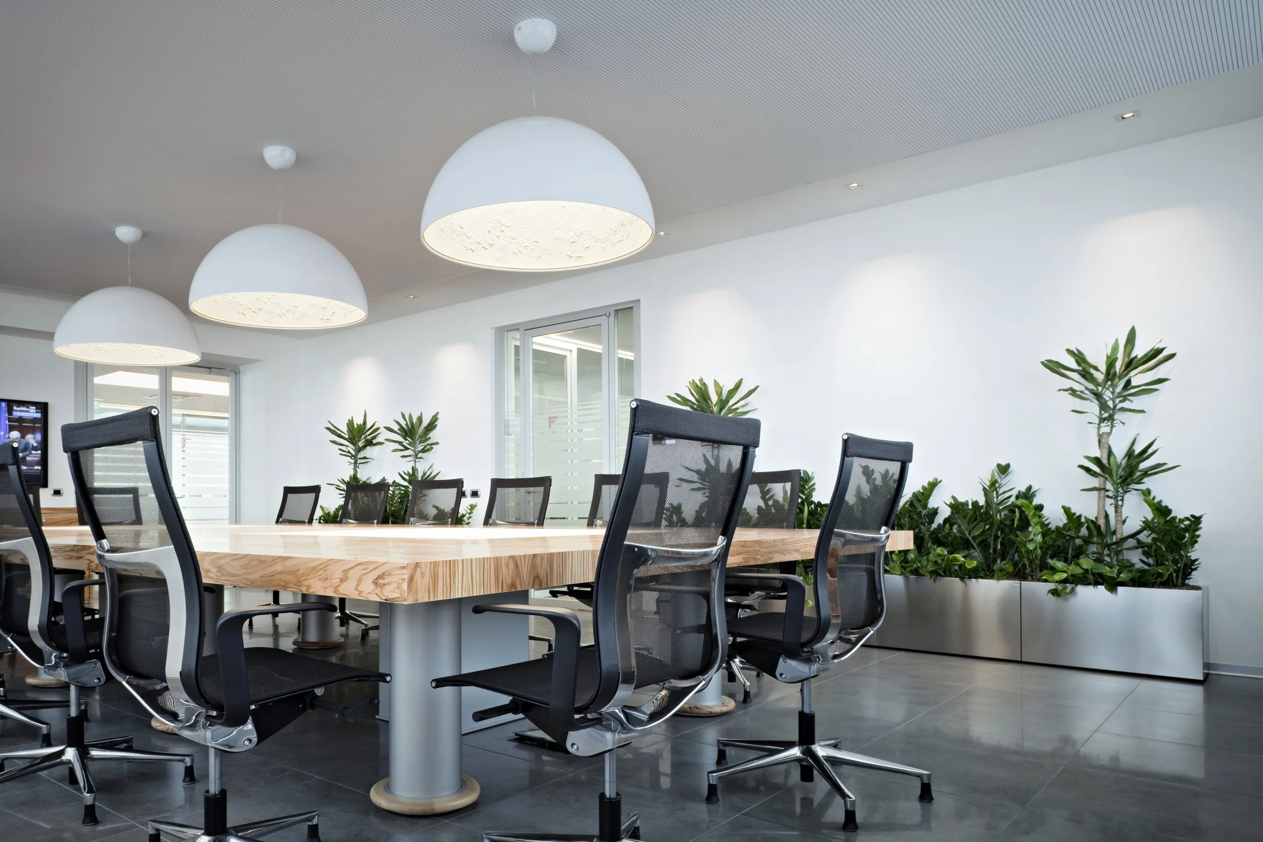 Conference room with a large wooden table, black mesh office chairs, and large, modern ceiling lights by FLOS.