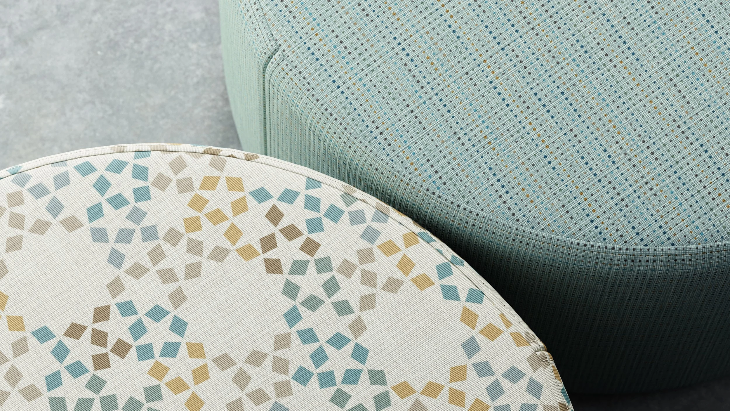 Close-up of two upholstered chairs with different geometric patterns from Designtex; one with blue, beige, and brown diamond shapes, and the other with a small multicolored dotted pattern.