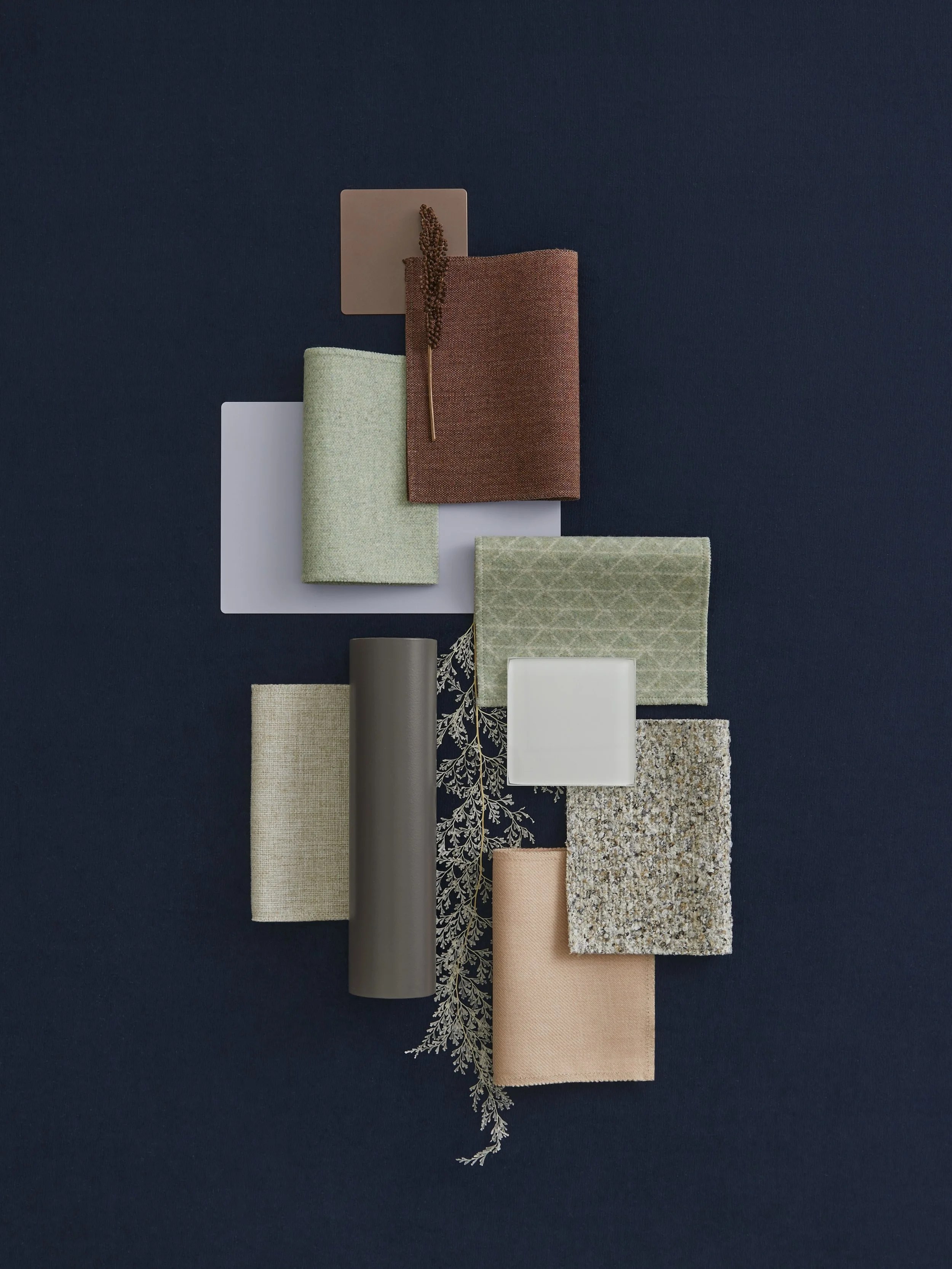 Arrangement of fabric swatches, a cylindrical object, a small square dish, a sprig of foliage, and a square tile on a dark background.
