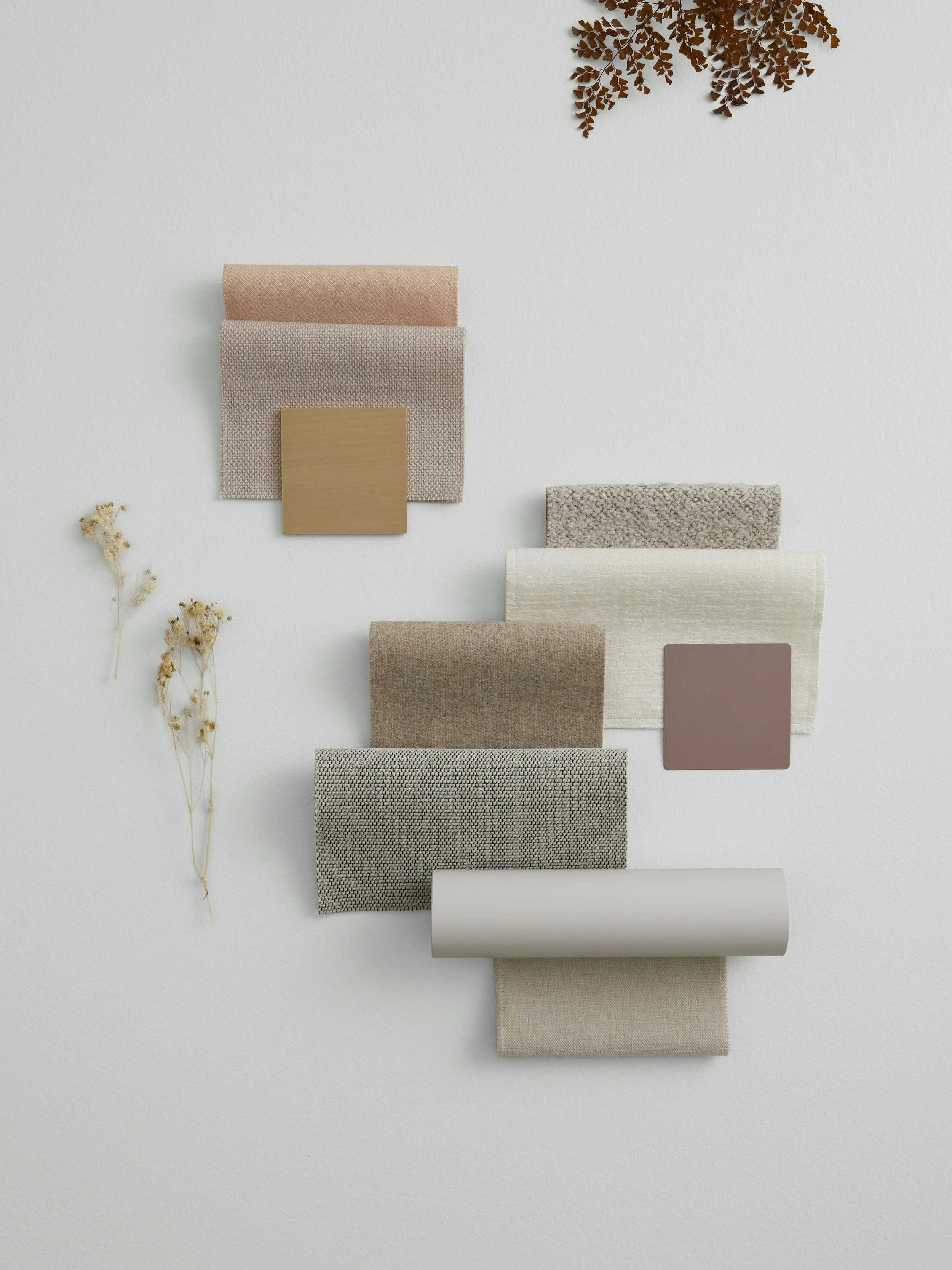 A collection of fabric swatches in neutral tones arranged on a white background, with small dried flowers and a brown leaf sprig nearby.