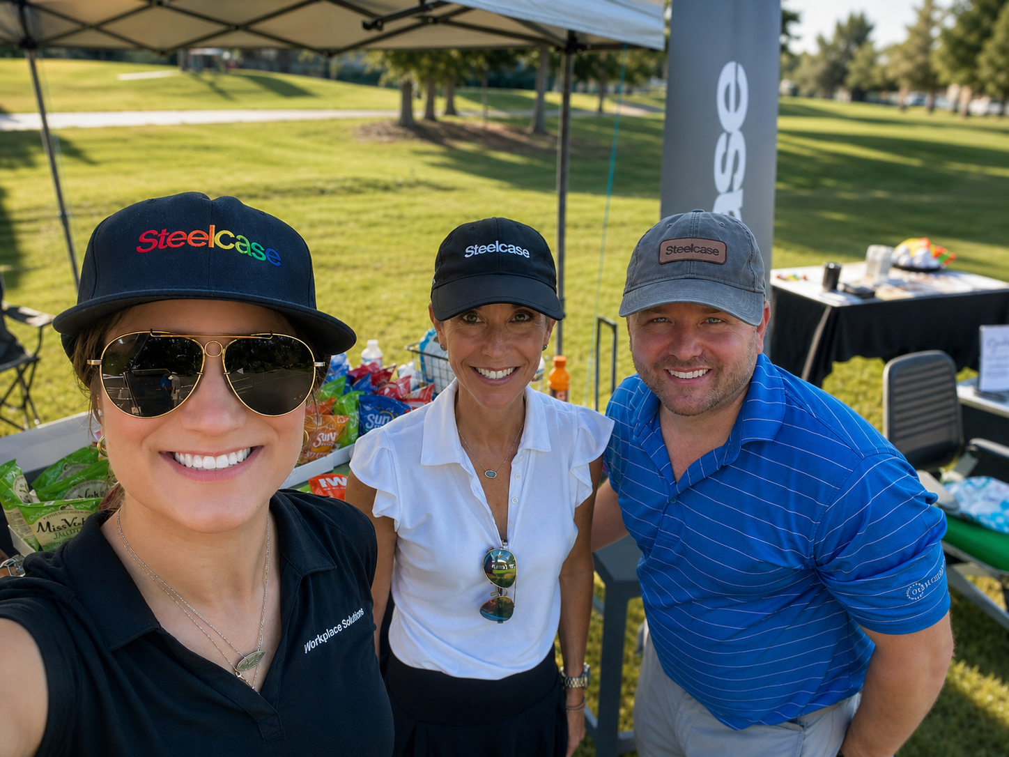 The Workplace Solutions and Steelcase team wearing Steelcase logo hats, taking a selfie under a canopy with snack tables at a corporate golf event.
