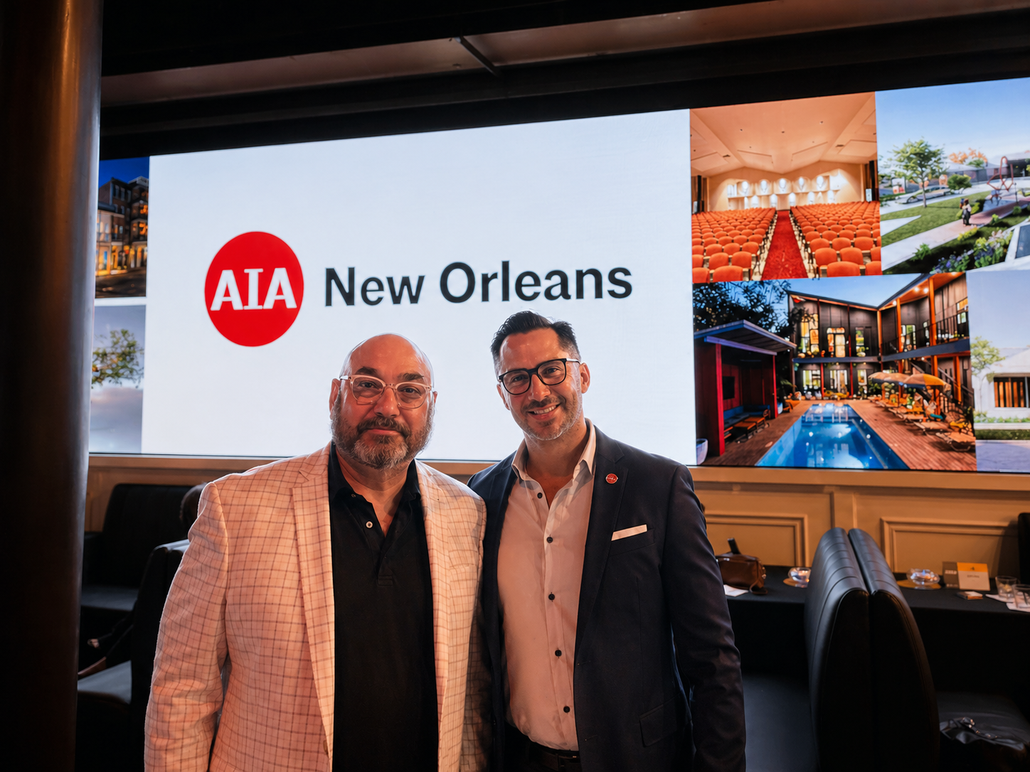 Paul Maczka and Francisco Morales from Workplace Solutions posing for a picture in front of a large screen displaying the AIA New Orleans logo and images at the 2024 AIA Awards event.