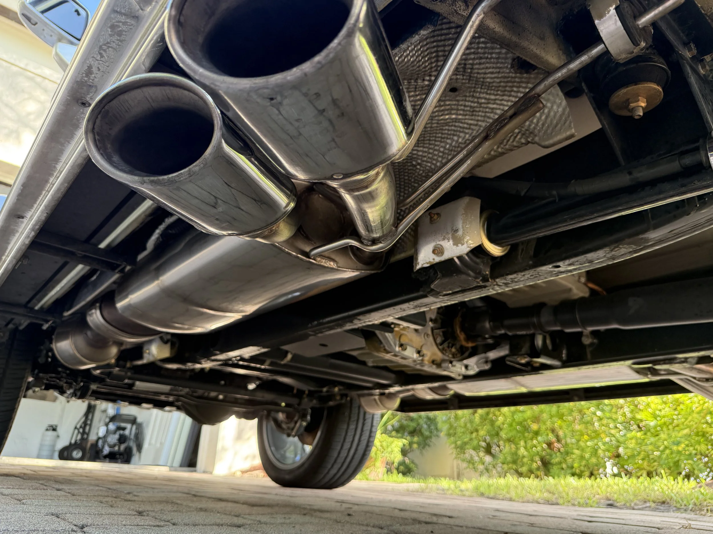 Underneath view of a car's exhaust system, showing dual exhaust pipes, muffler, and various undercarriage components.