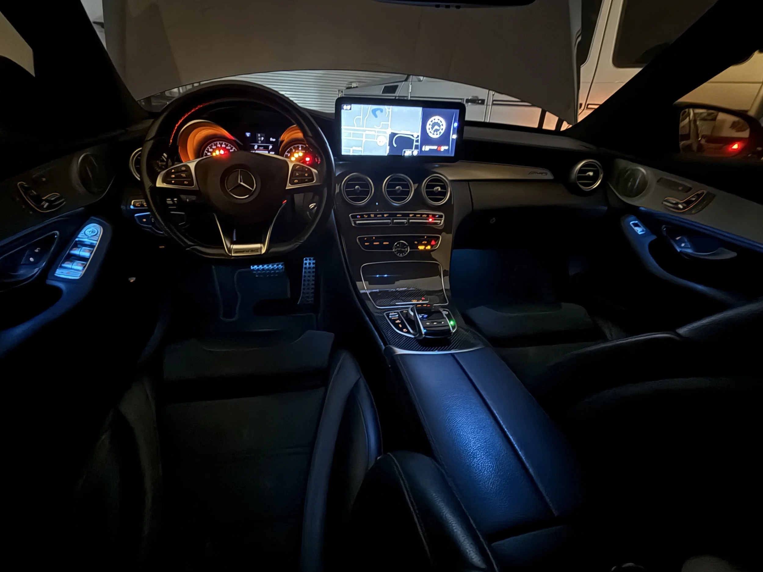 Interior of a luxury Mercedes-Benz car with illuminated dashboard, steering wheel, and center console, featuring a large digital display screen showing a navigation map.