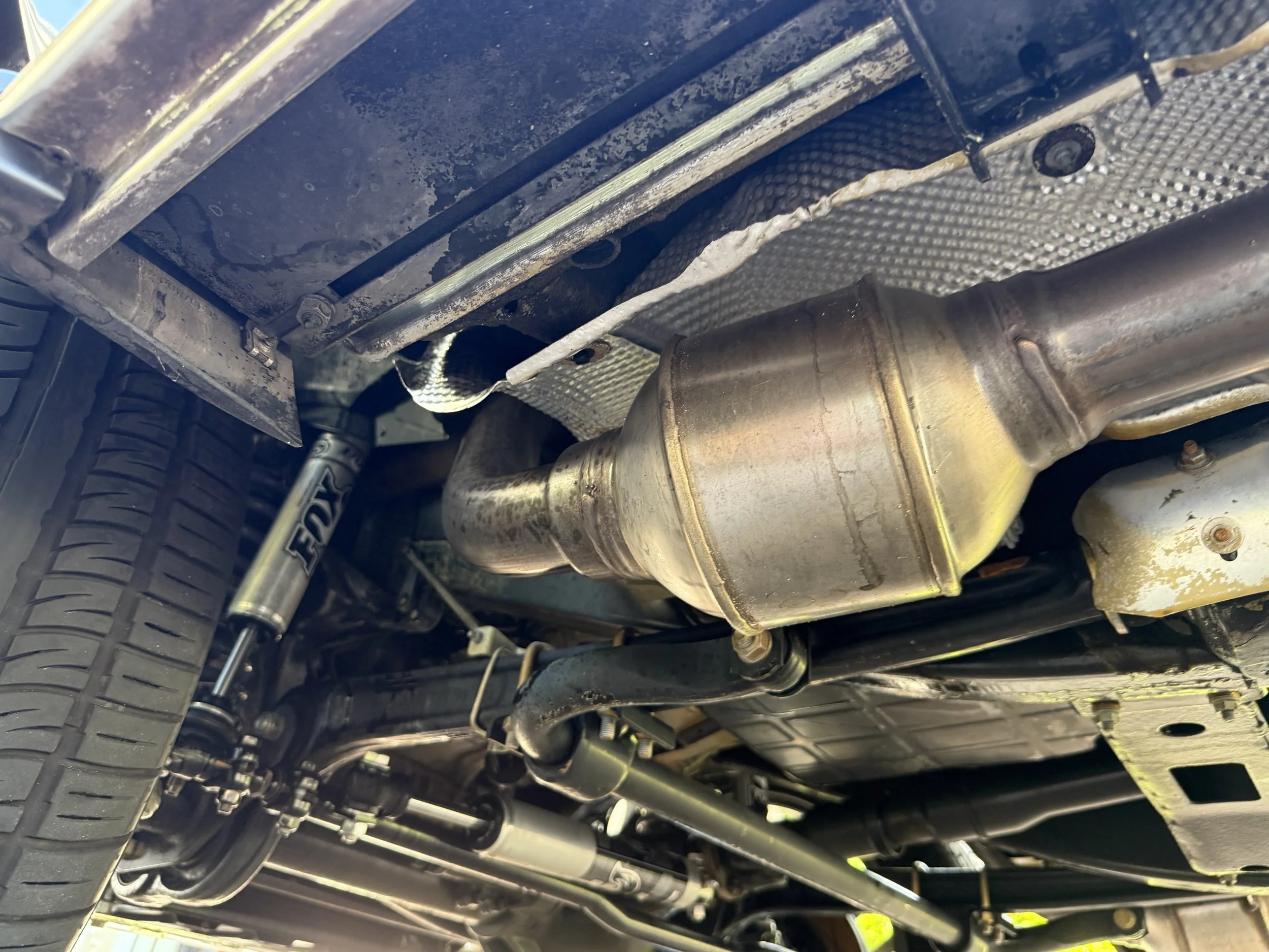 Underneath view of a car showing the exhaust system, suspension components, and wheel with tire.