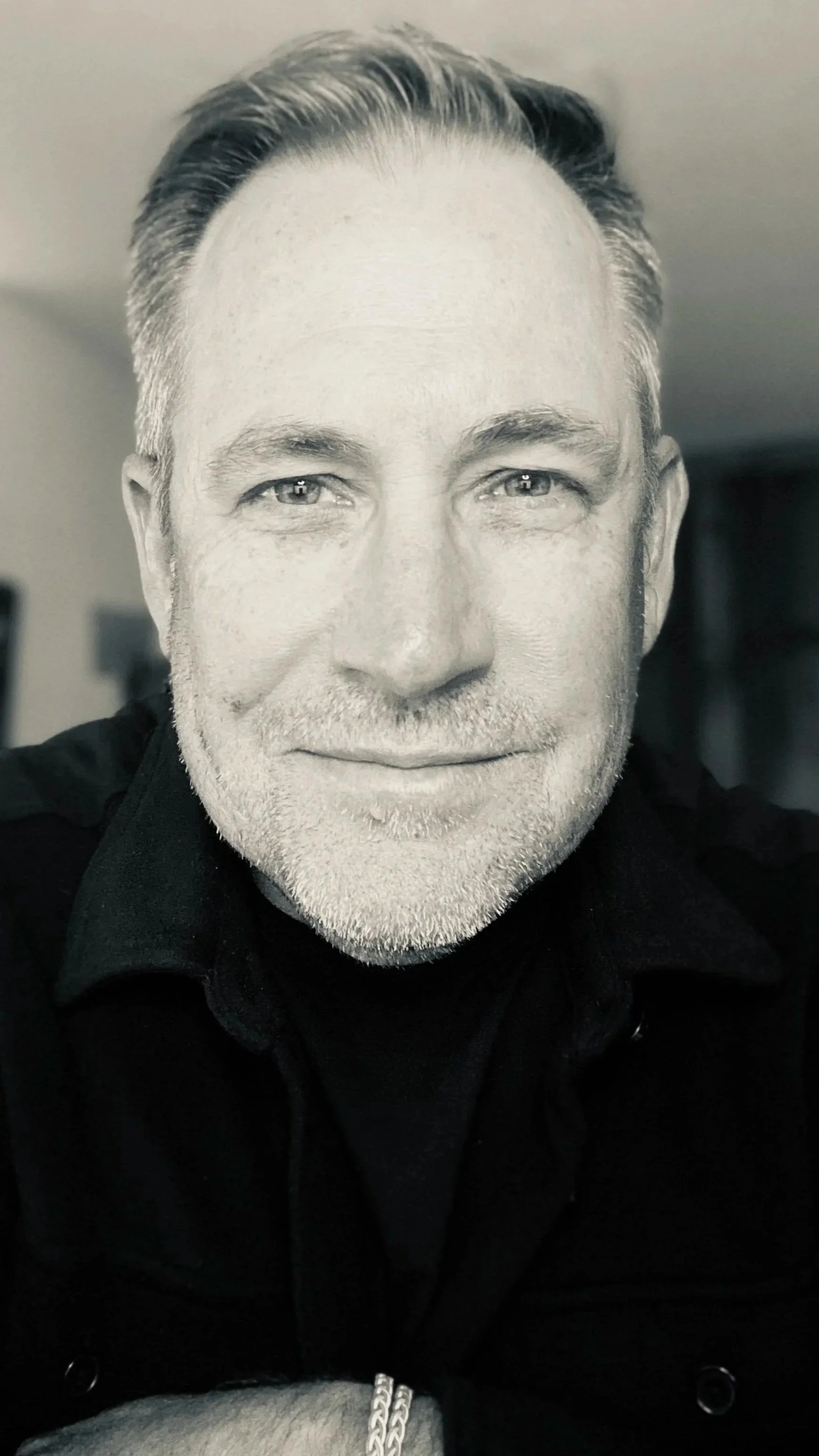A black-and-white close-up portrait of a middle-aged man with light-colored hair, a beard, and a mustache, smiling slightly and looking into the camera.