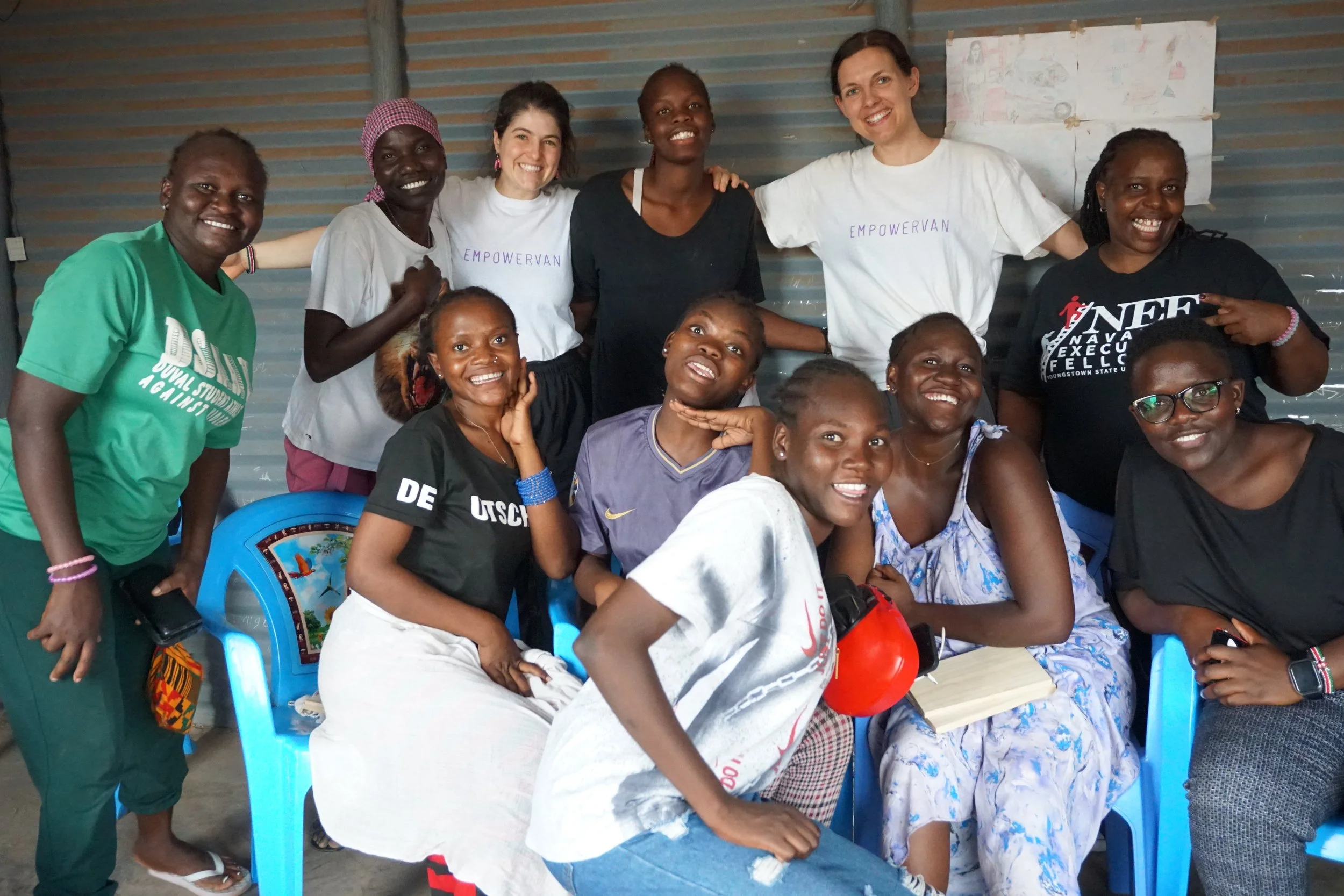 Ten people standing outdoors facing a white wall, holding up wooden plaques, with trees and a streetlamp illuminating the scene in the background.